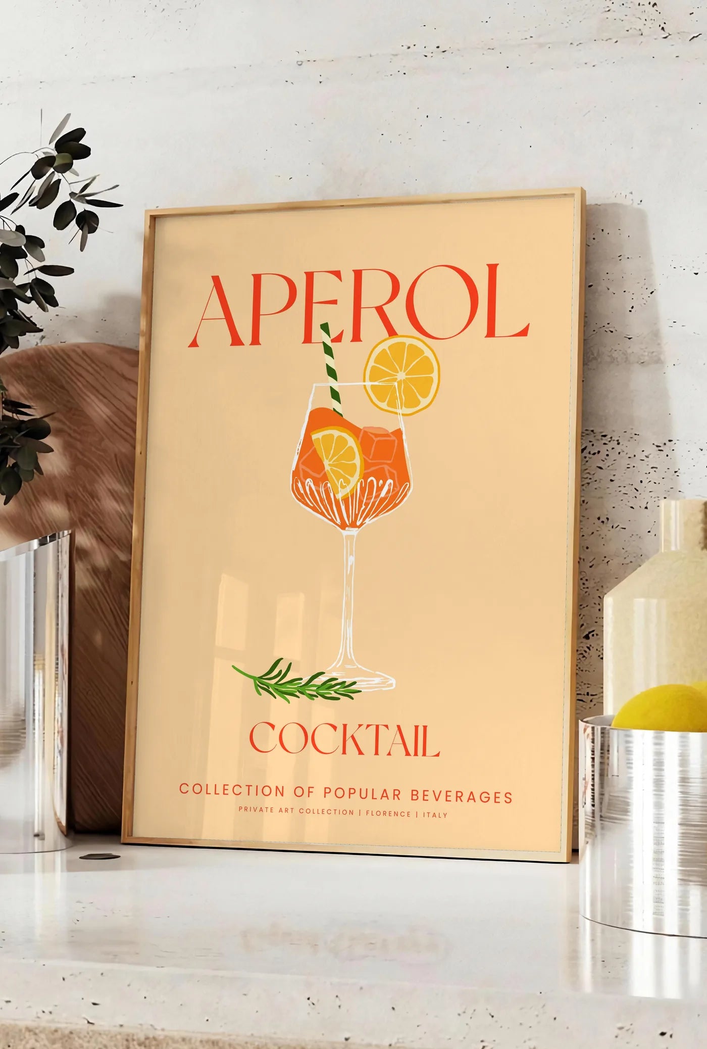 Affiche affiche cocktail Aperol Spritz, posee sur un plan de travail de cuisine en pierre claire, entre une branche d'eucalyptus en vase et un bocal de citrons