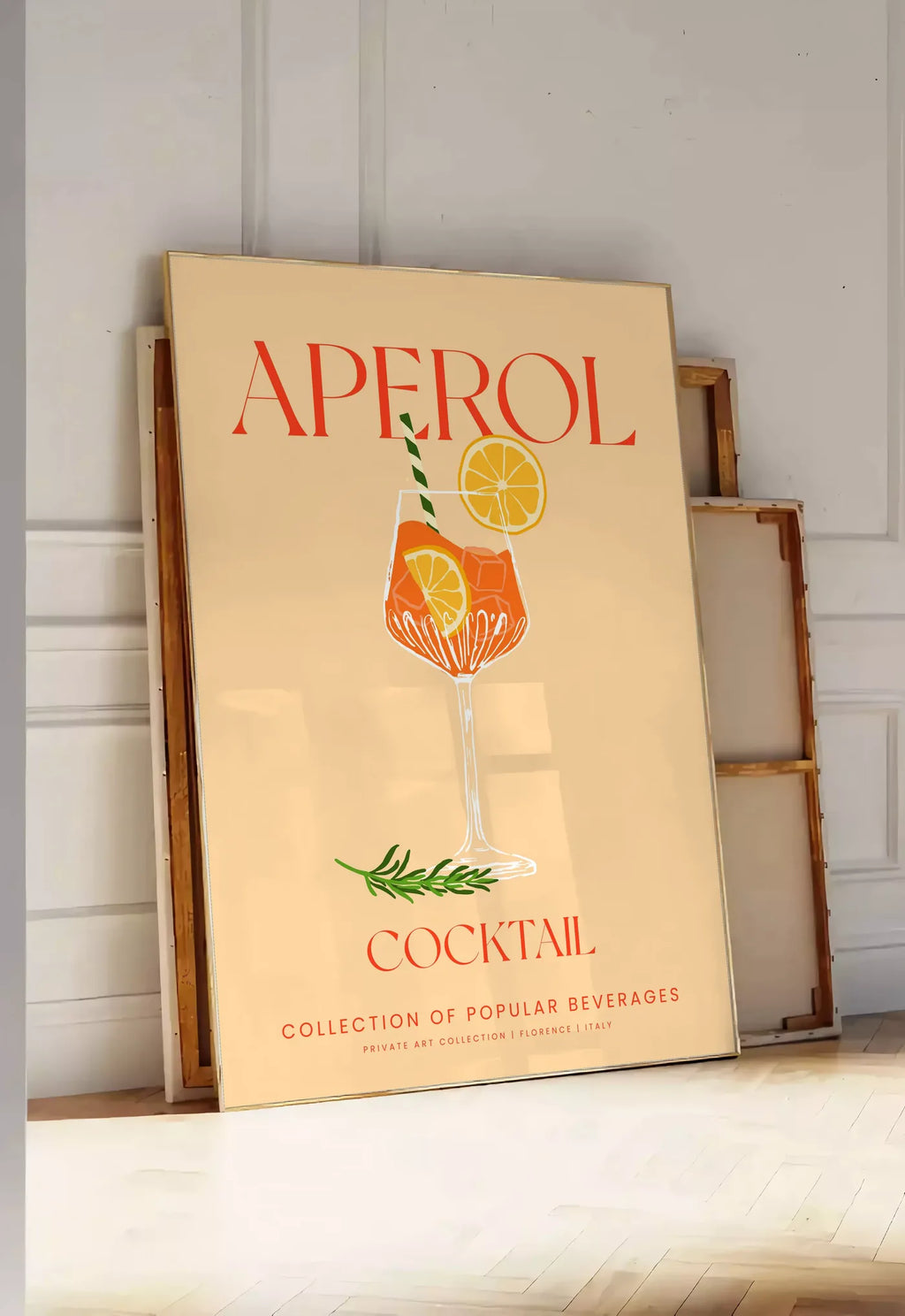 Tirage encadrable affiche cocktail Aperol Spritz, posee au sol dans une entree lumineuse, contre un mur a panneaux blancs, a cote de chassis en bois empiles