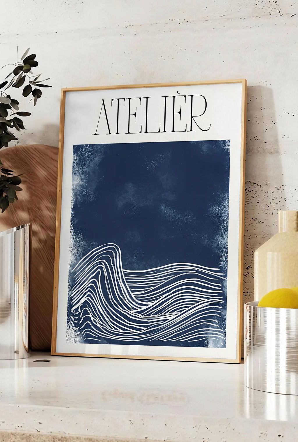 Affiche affiche Atelier vagues minimaliste, posee sur un plan de travail de cuisine en pierre claire, entre une branche d'eucalyptus en vase et un bocal de citrons