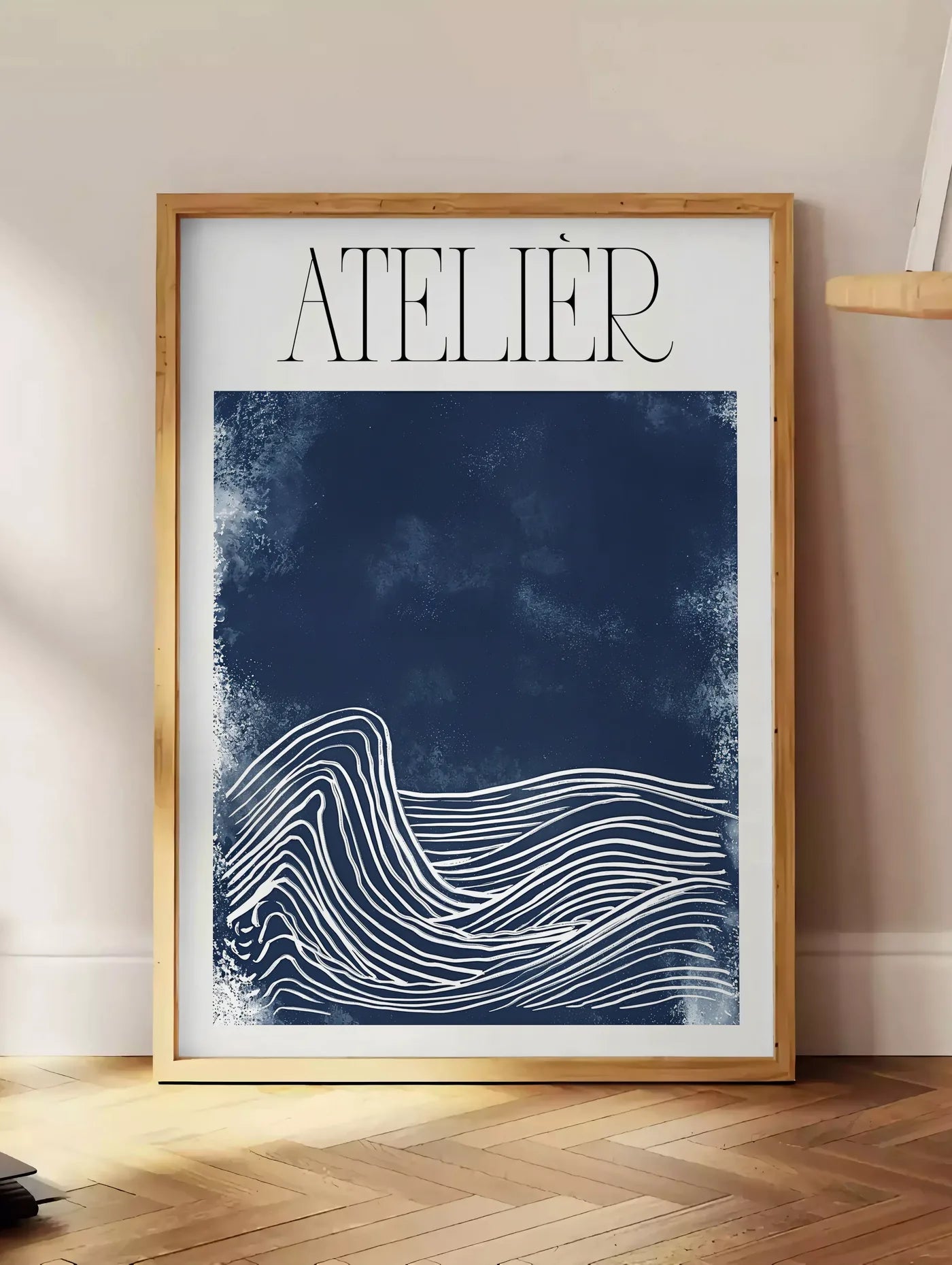 Estampe affiche Atelier vagues minimaliste, posee au sol dans un coin salon, sur un parquet a chevrons, pres d'une table d'appoint en chene chargee de livres