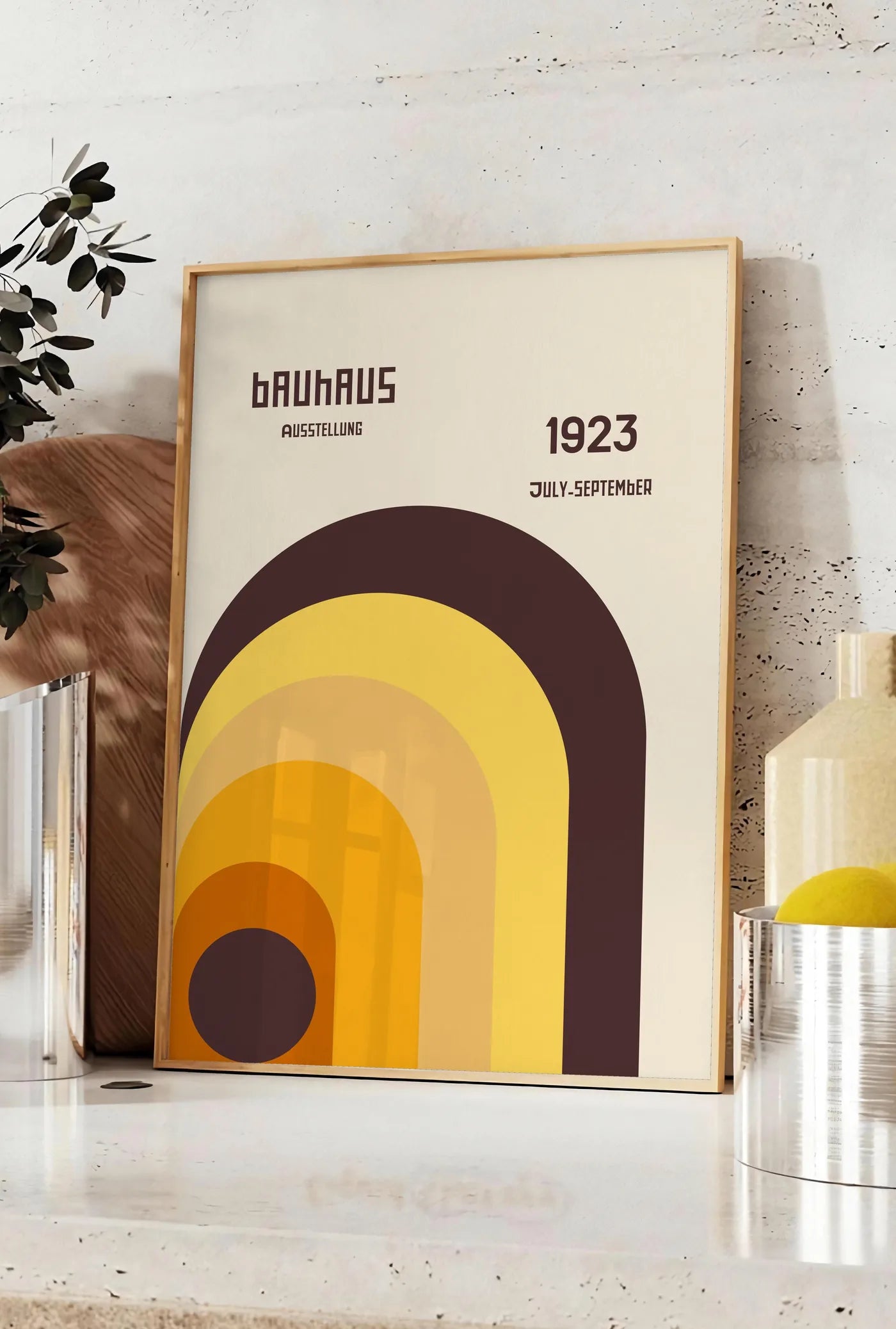 Affiche arche Orange, posee sur un plan de travail de cuisine en pierre claire, entre une branche d'eucalyptus en vase et un bocal de citrons