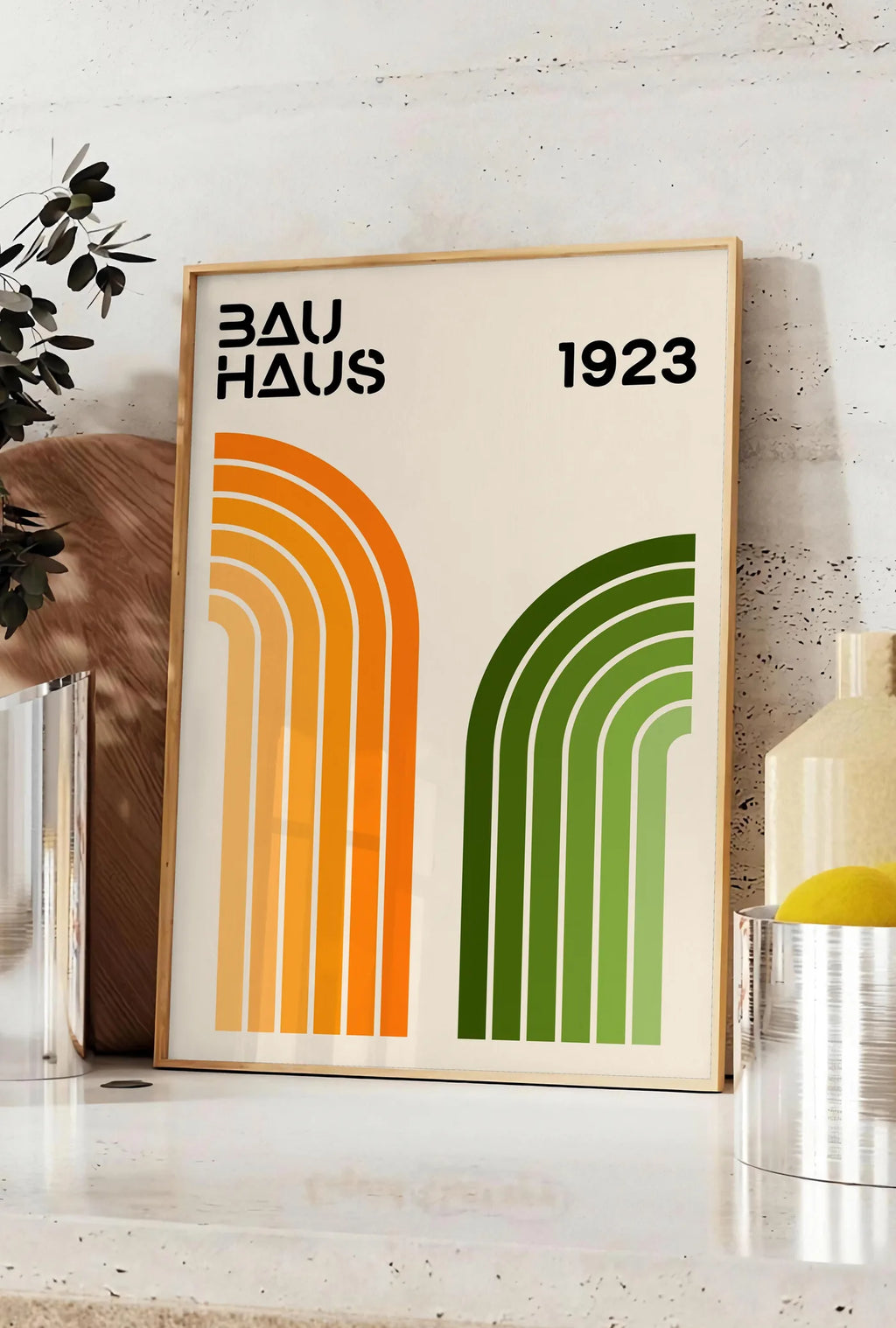 Affiche arches Orange et Vert, posee sur un plan de travail de cuisine en pierre claire, entre une branche d'eucalyptus en vase et un bocal de citrons