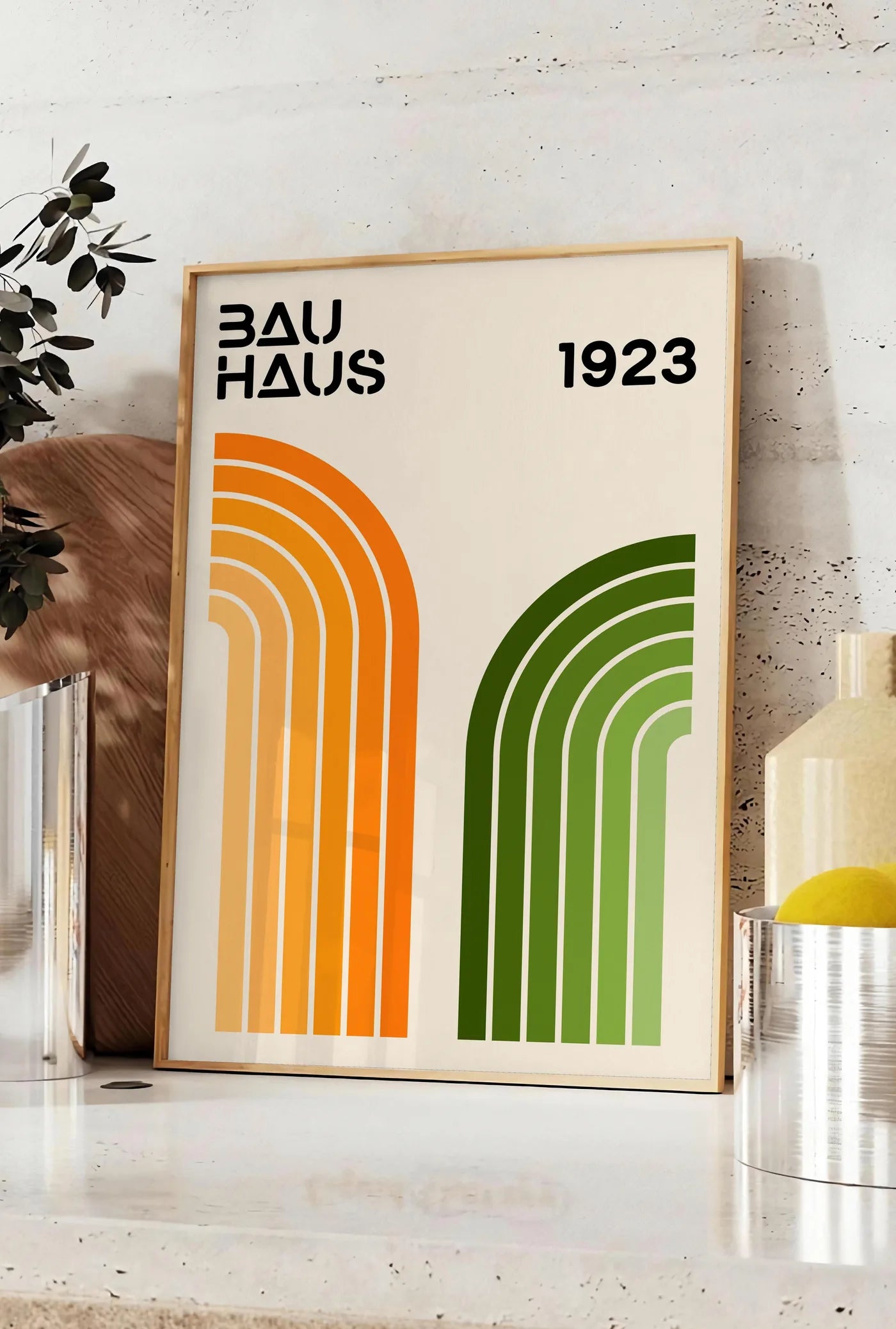Affiche arches Orange et Vert, posee sur un plan de travail de cuisine en pierre claire, entre une branche d'eucalyptus en vase et un bocal de citrons
