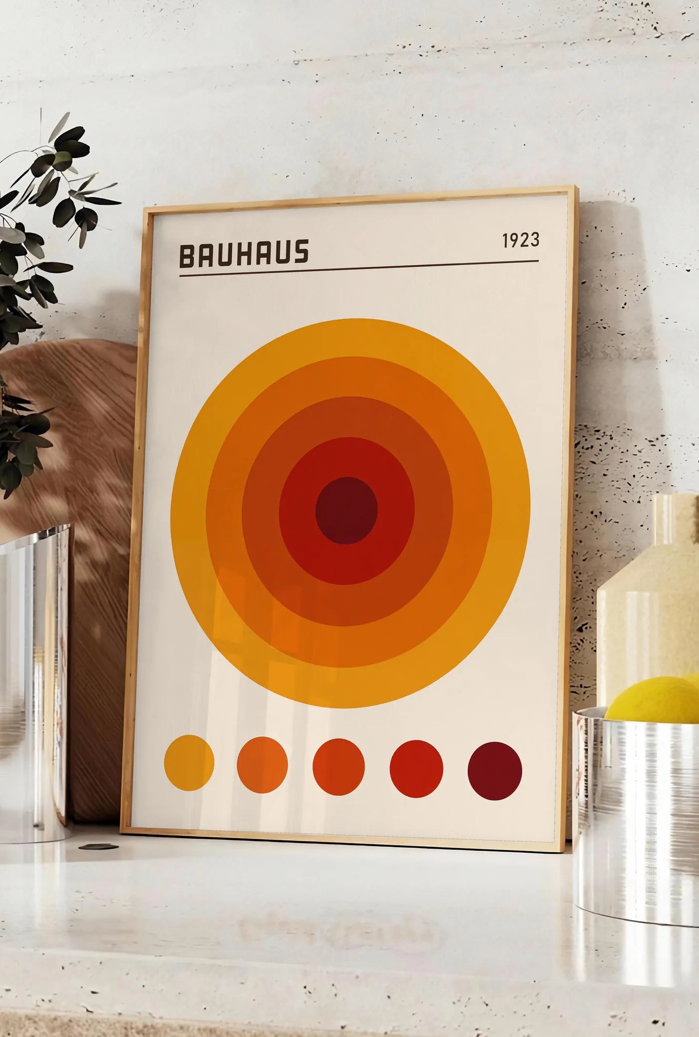 Affiche cercles Concentriques Orange, posee sur un plan de travail de cuisine en pierre claire, entre une branche d'eucalyptus en vase et un bocal de citrons