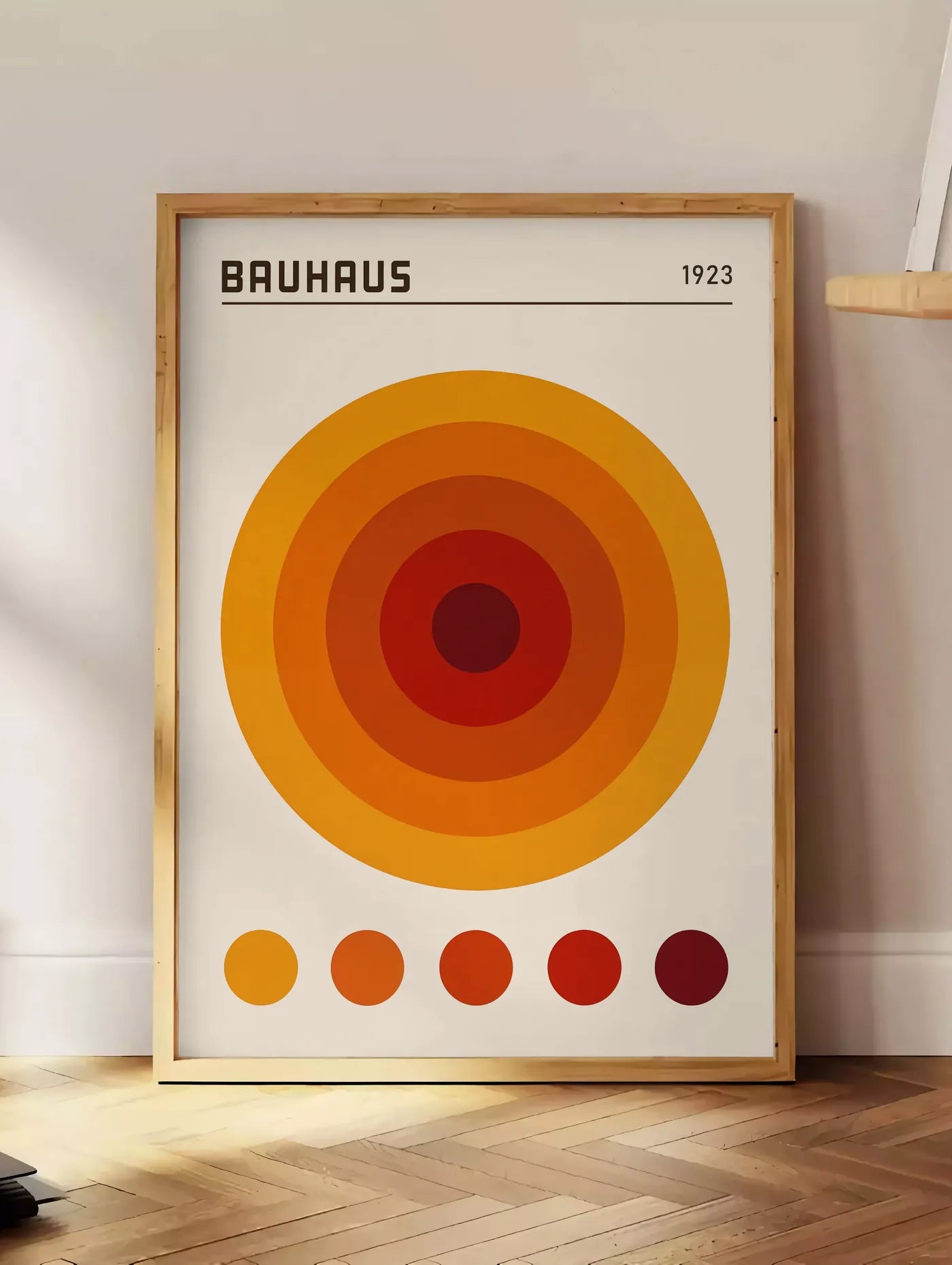 Estampe cercles Concentriques Orange, posee au sol dans un coin salon, sur un parquet a chevrons, pres d'une table d'appoint en chene chargee de livres