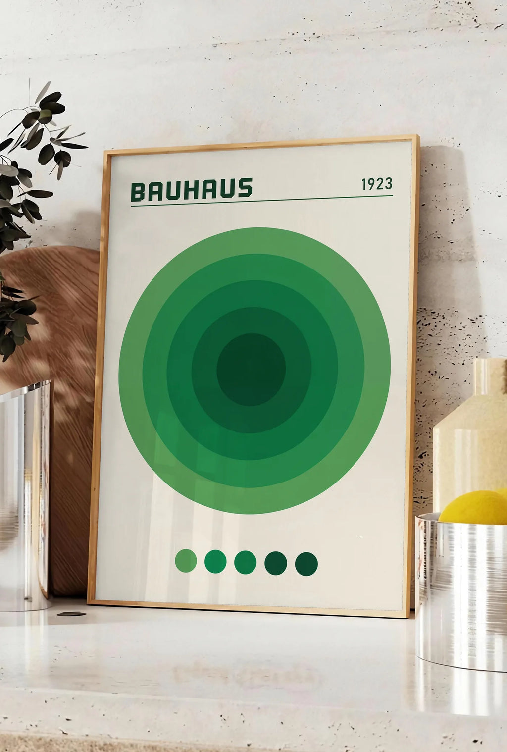 Affiche cercles Concentriques Verts, posee sur un plan de travail de cuisine en pierre claire, entre une branche d'eucalyptus en vase et un bocal de citrons