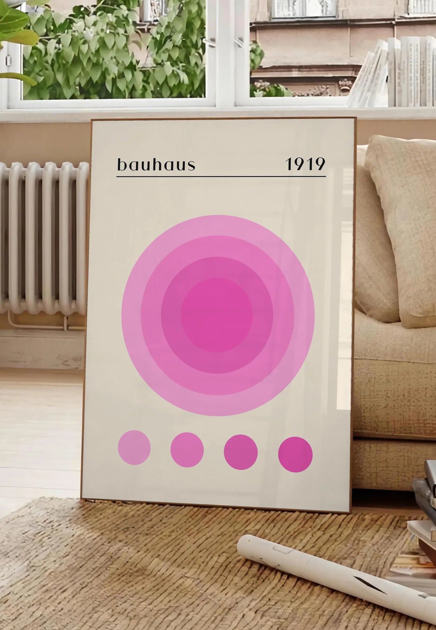 Poster affiche Bauhaus 1919, posee au sol dans un salon parisien, devant une grande fenetre donnant sur un immeuble haussmannien, entre un ficus et un canape creme