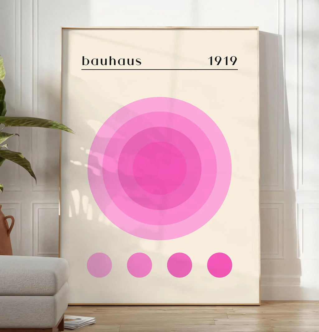 Reproduction affiche Bauhaus 1919, posee au sol dans un salon minimaliste clair, a cote d'un canape beige et d'une plante verte, sur un parquet clair