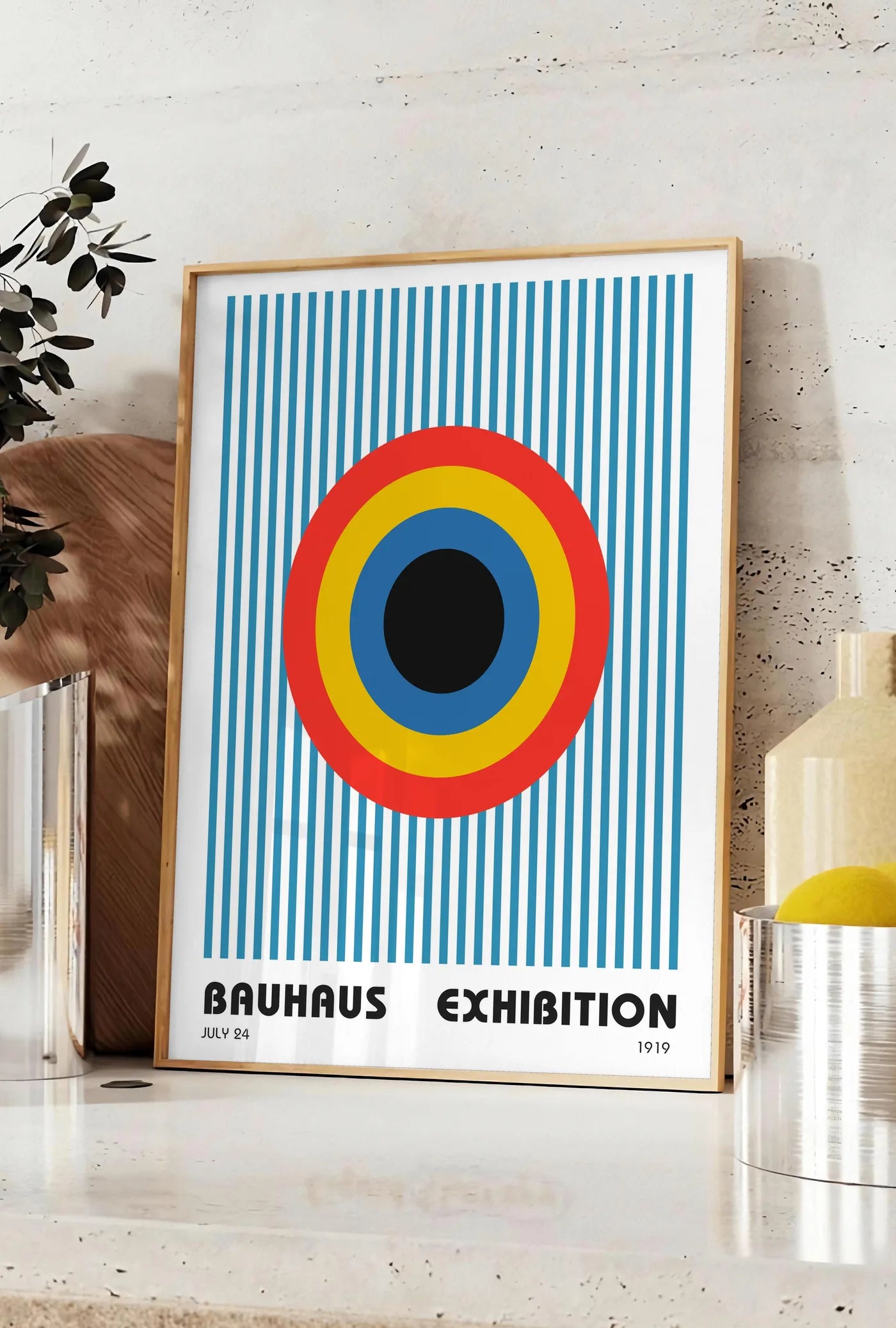 Affiche cible et Rayures, posee sur un plan de travail de cuisine en pierre claire, entre une branche d'eucalyptus en vase et un bocal de citrons