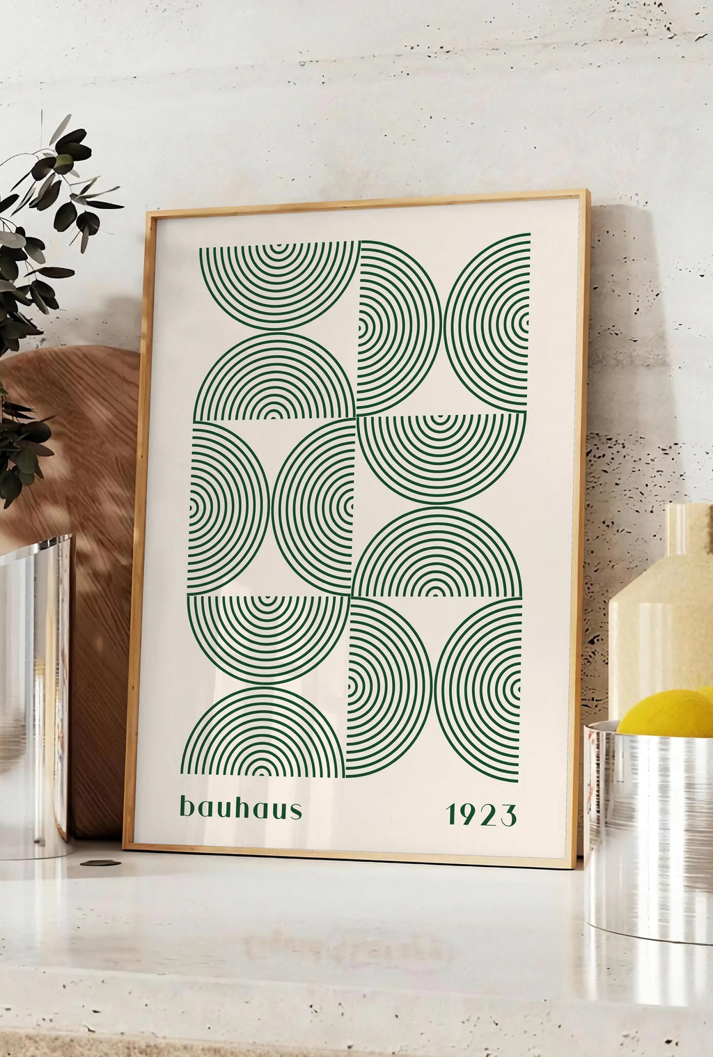 Affiche arcs Concentriques Verts, posee sur un plan de travail de cuisine en pierre claire, entre une branche d'eucalyptus en vase et un bocal de citrons