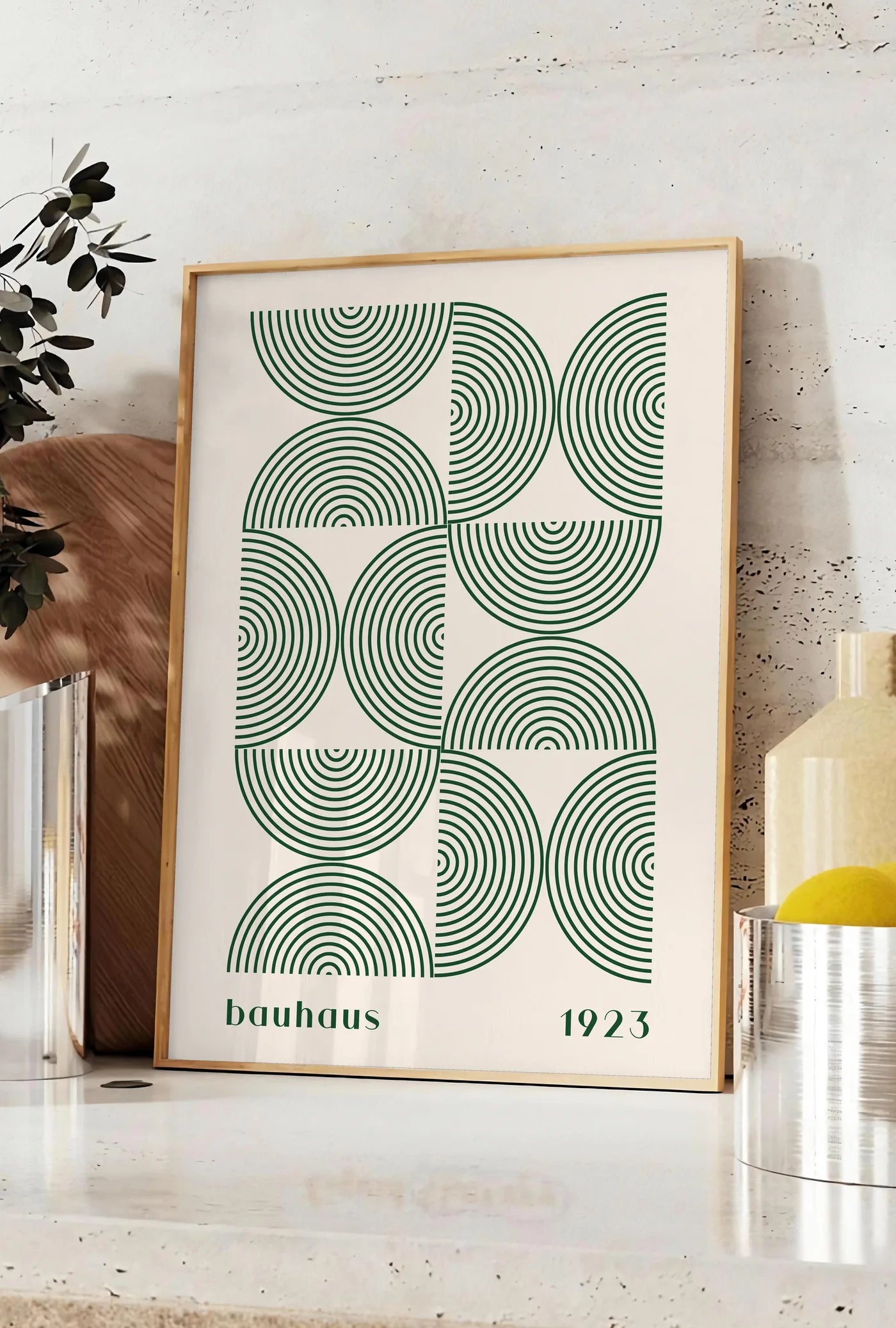 Affiche arcs Concentriques Verts, posee sur un plan de travail de cuisine en pierre claire, entre une branche d'eucalyptus en vase et un bocal de citrons