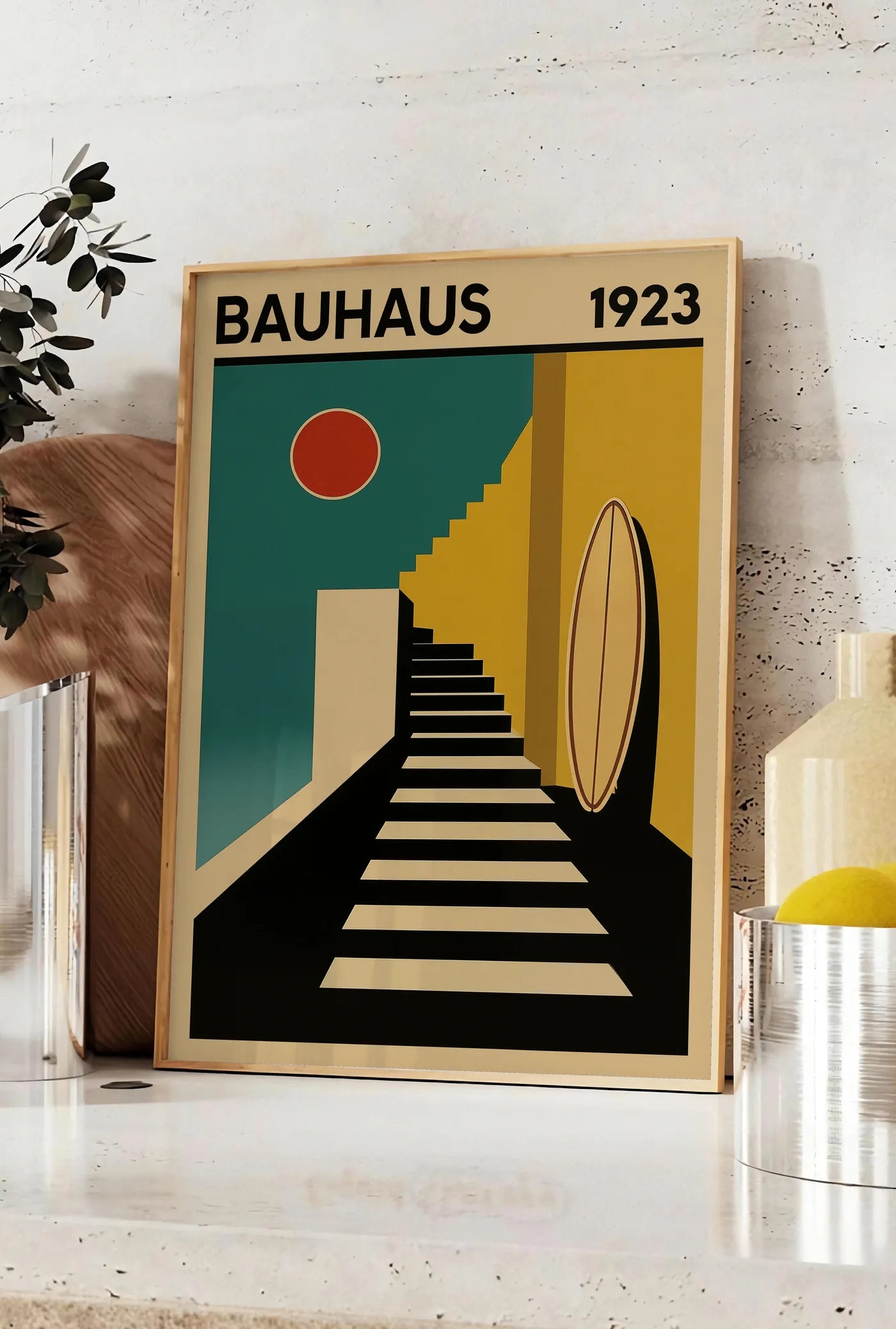 Affiche escalier et Surf, posee sur un plan de travail de cuisine en pierre claire, entre une branche d'eucalyptus en vase et un bocal de citrons