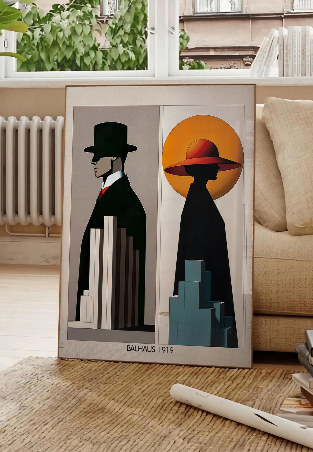 Poster figures Art Deco, posee au sol dans un salon parisien, devant une grande fenetre donnant sur un immeuble haussmannien, entre un ficus et un canape creme