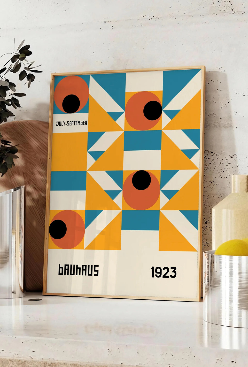 Affiche grille aux Yeux Orange, posee sur un plan de travail de cuisine en pierre claire, entre une branche d'eucalyptus en vase et un bocal de citrons