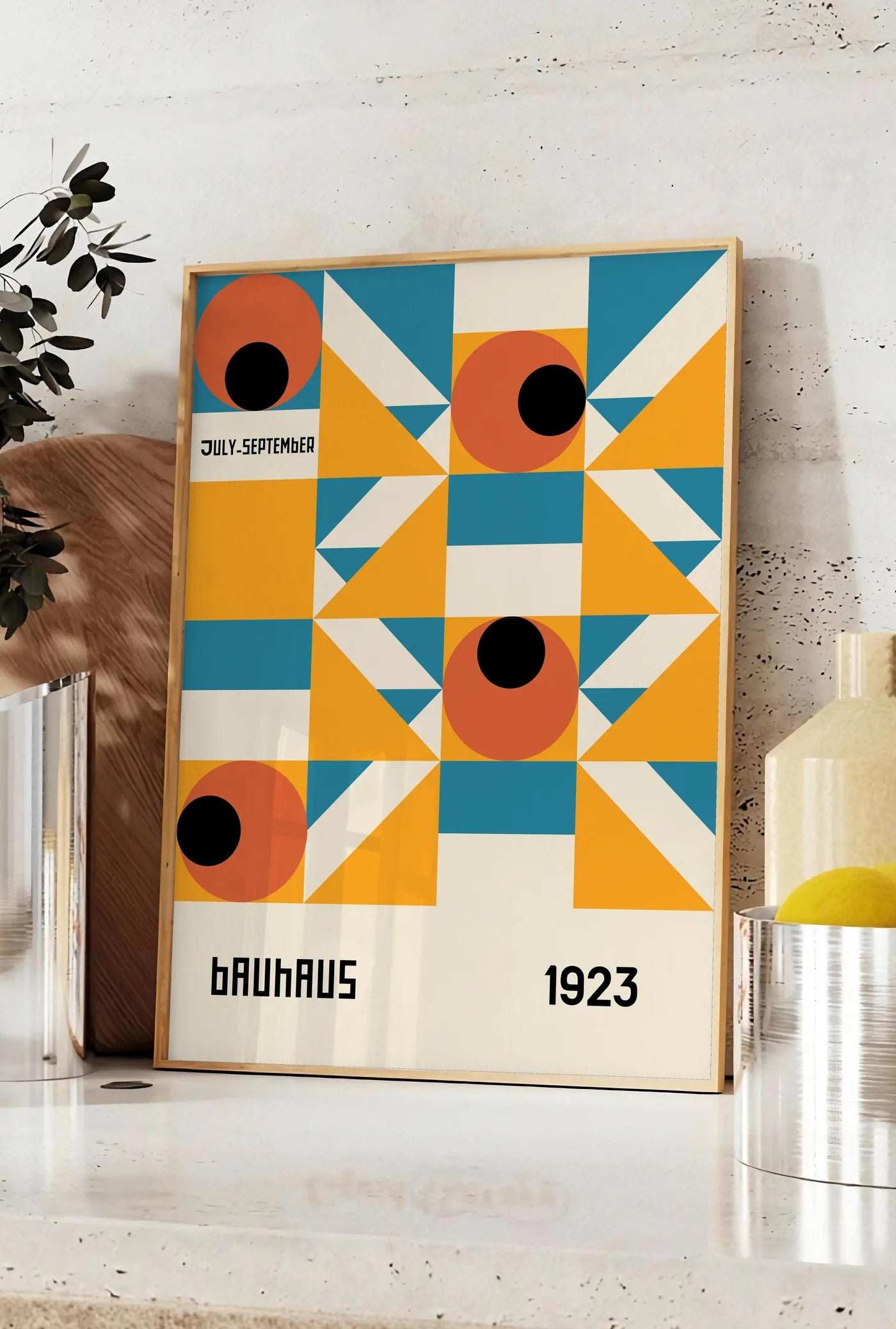 Affiche grille aux Yeux Orange, posee sur un plan de travail de cuisine en pierre claire, entre une branche d'eucalyptus en vase et un bocal de citrons