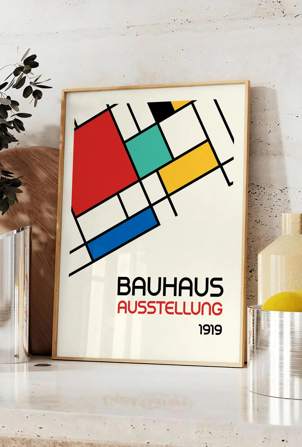 Affiche blocs Mondrian, posee sur un plan de travail de cuisine en pierre claire, entre une branche d'eucalyptus en vase et un bocal de citrons