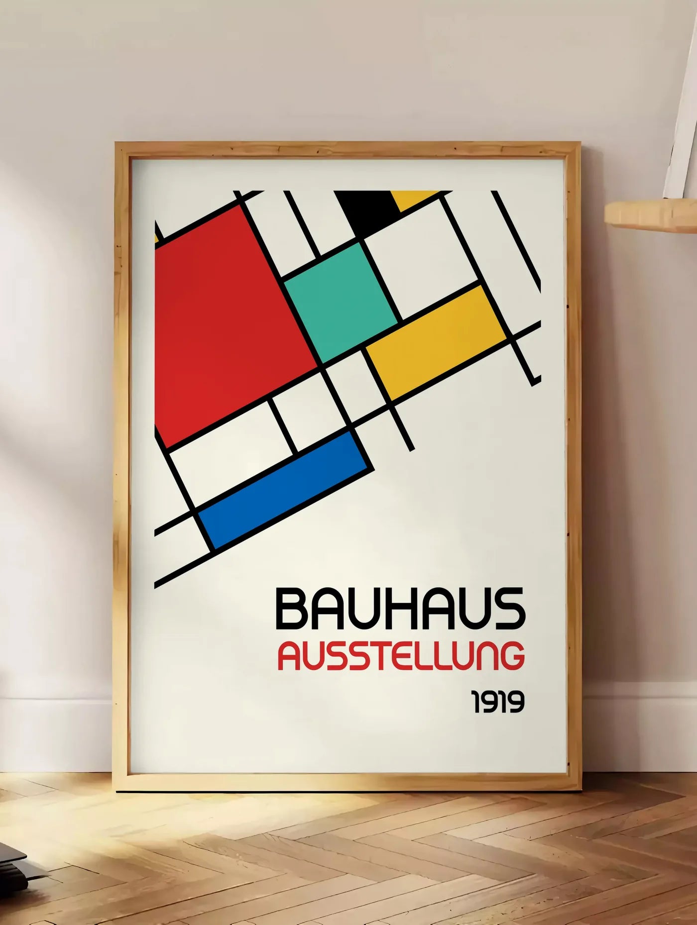 Estampe blocs Mondrian, posee au sol dans un coin salon, sur un parquet a chevrons, pres d'une table d'appoint en chene chargee de livres