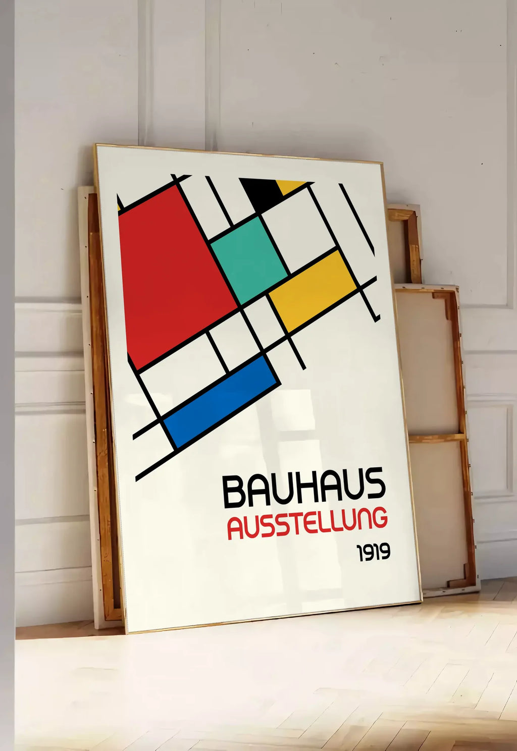Tirage encadrable blocs Mondrian, posee au sol dans une entree lumineuse, contre un mur a panneaux blancs, a cote de chassis en bois empiles