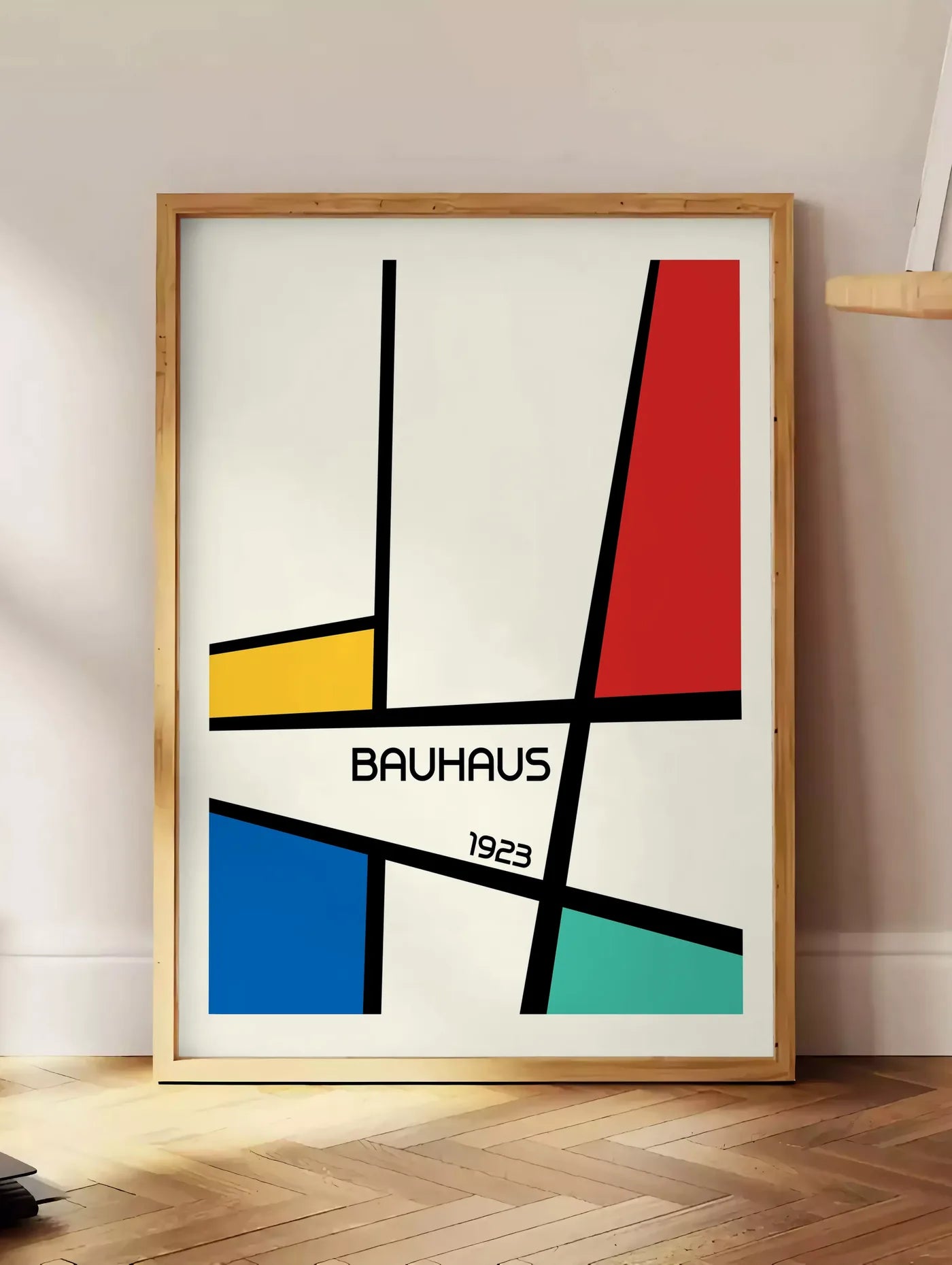 Estampe mondrian Diagonal, posee au sol dans un coin salon, sur un parquet a chevrons, pres d'une table d'appoint en chene chargee de livres