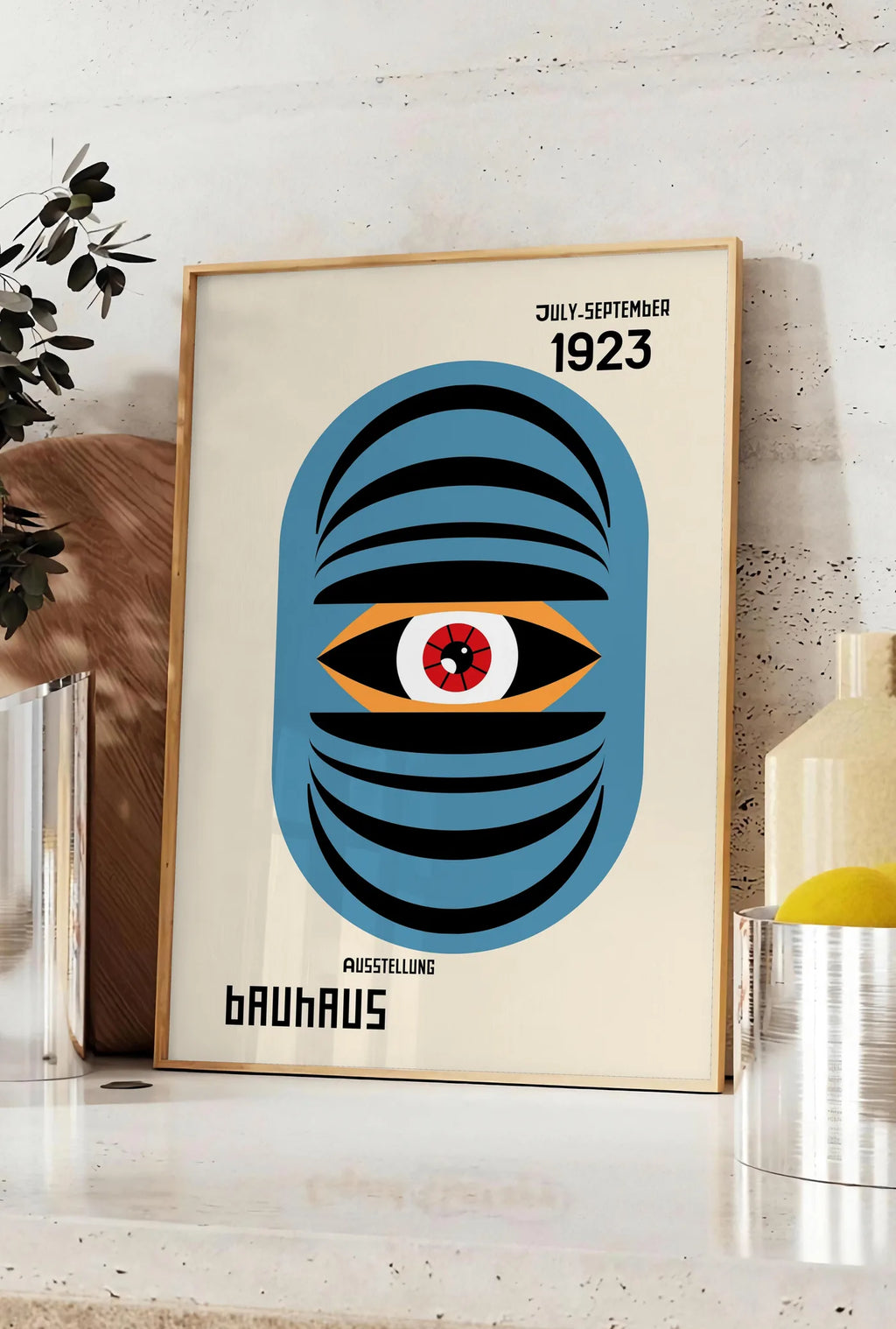 Affiche oeil Bleu Surreel, posee sur un plan de travail de cuisine en pierre claire, entre une branche d'eucalyptus en vase et un bocal de citrons