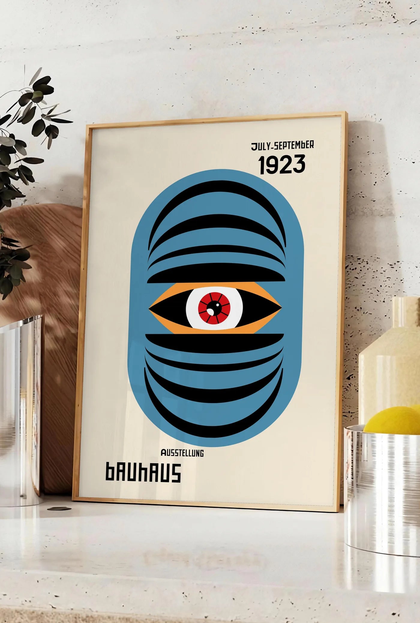 Affiche oeil Bleu Surreel, posee sur un plan de travail de cuisine en pierre claire, entre une branche d'eucalyptus en vase et un bocal de citrons