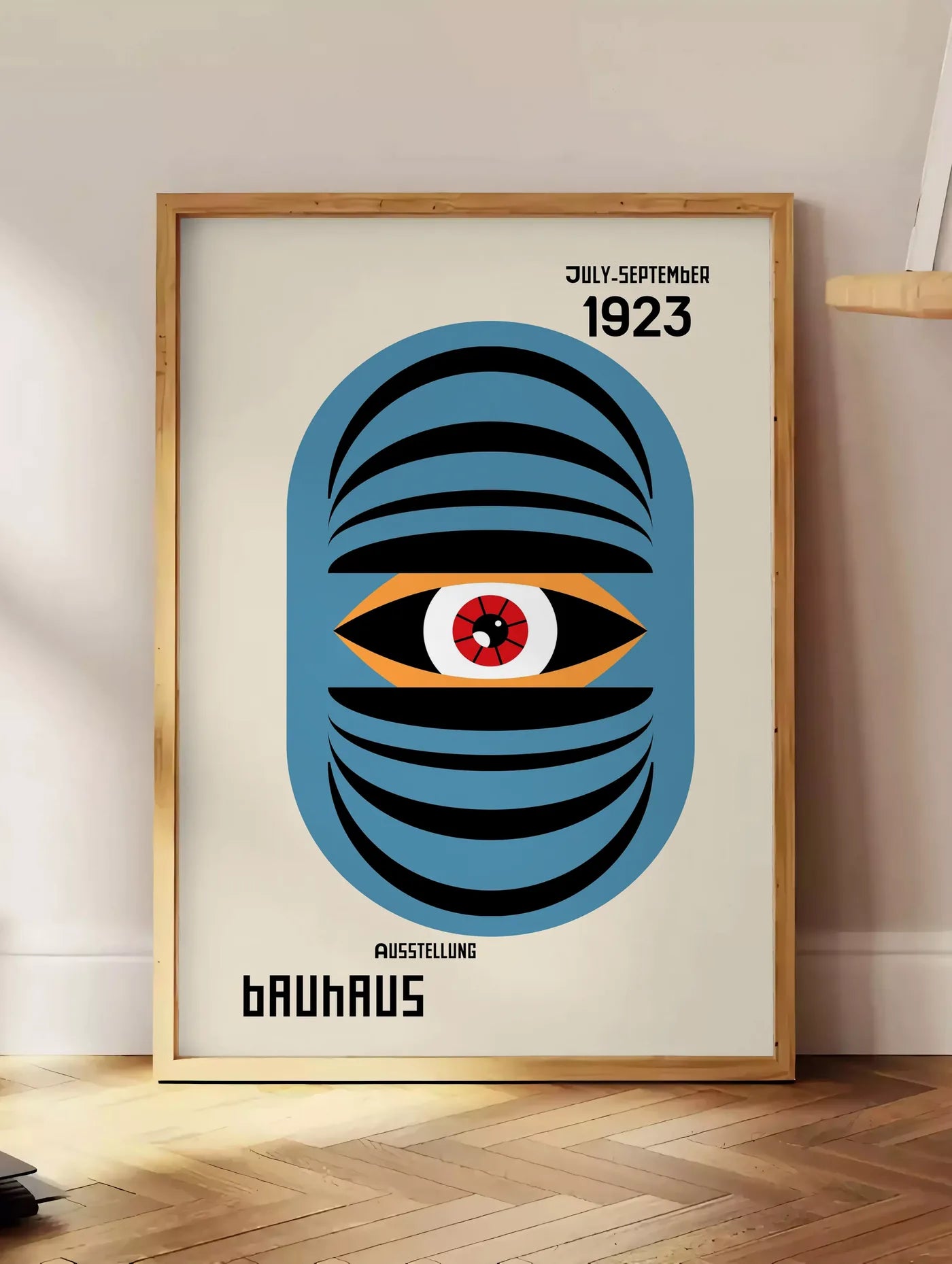 Estampe oeil Bleu Surreel, posee au sol dans un coin salon, sur un parquet a chevrons, pres d'une table d'appoint en chene chargee de livres