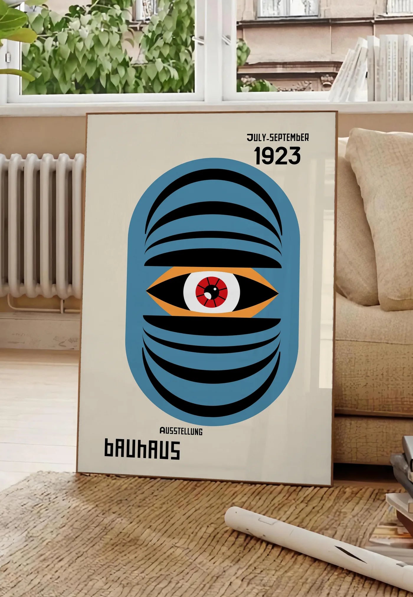 Poster oeil Bleu Surreel, posee au sol dans un salon parisien, devant une grande fenetre donnant sur un immeuble haussmannien, entre un ficus et un canape creme