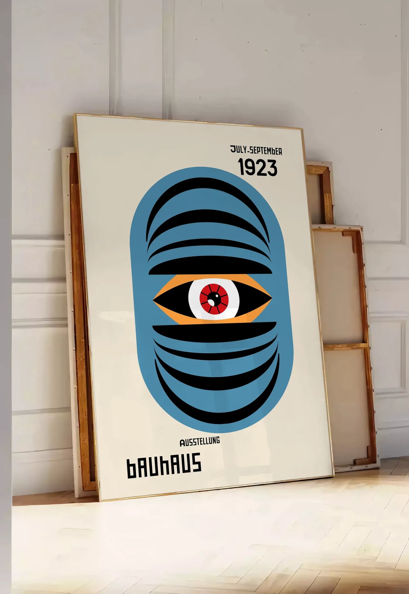 Tirage encadrable oeil Bleu Surreel, posee au sol dans une entree lumineuse, contre un mur a panneaux blancs, a cote de chassis en bois empiles