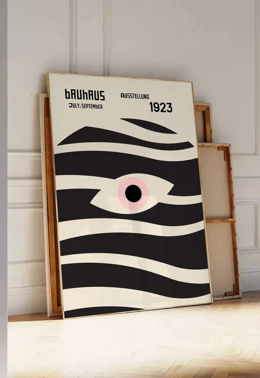 Tirage encadrable oeil et Vagues, posee au sol dans une entree lumineuse, contre un mur a panneaux blancs, a cote de chassis en bois empiles