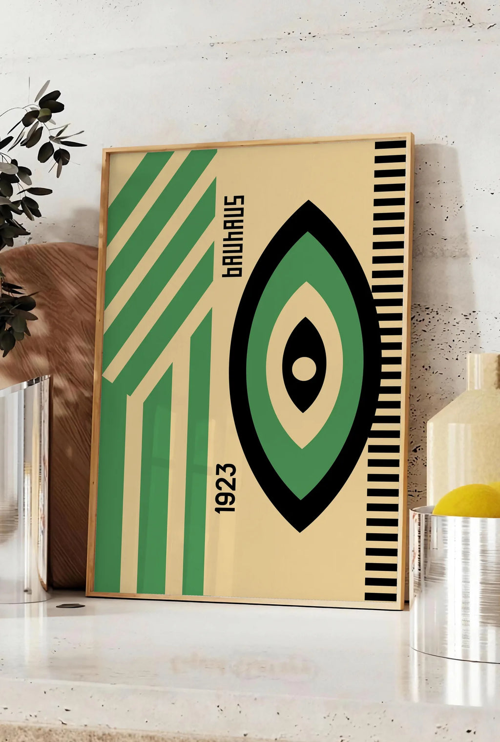 Affiche oeil Vert et Noir, posee sur un plan de travail de cuisine en pierre claire, entre une branche d'eucalyptus en vase et un bocal de citrons