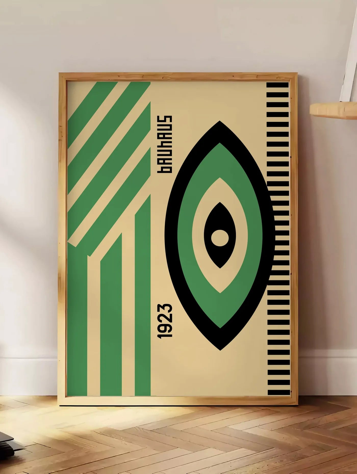 Estampe oeil Vert et Noir, posee au sol dans un coin salon, sur un parquet a chevrons, pres d'une table d'appoint en chene chargee de livres