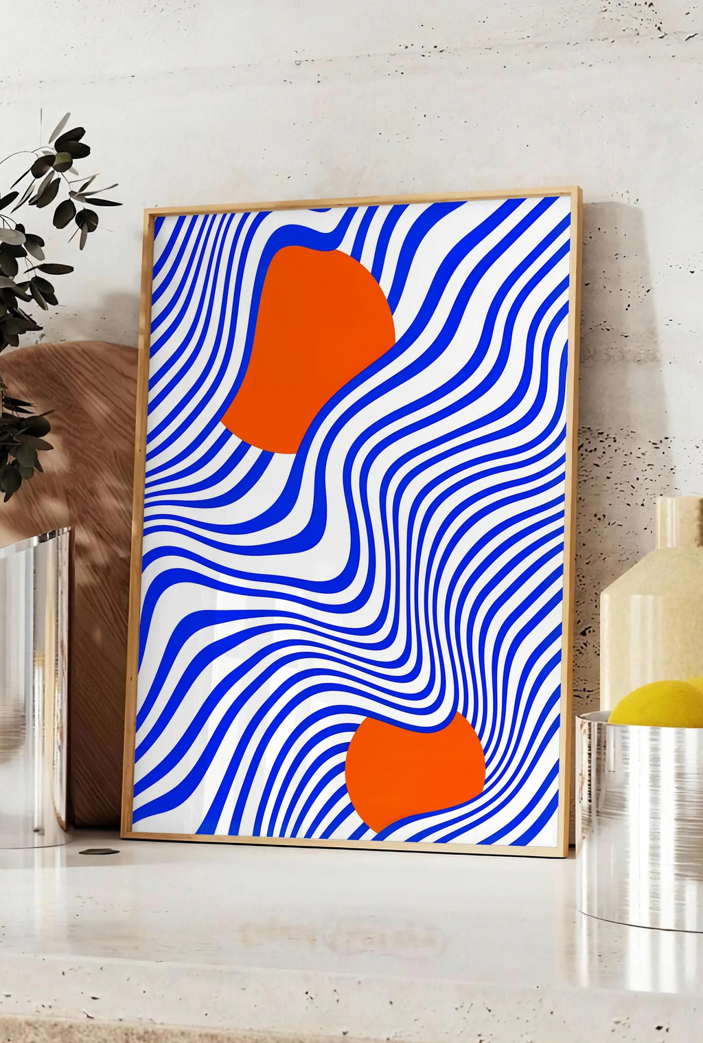 Affiche op Art Bleu et Orange, posee sur un plan de travail de cuisine en pierre claire, entre une branche d'eucalyptus en vase et un bocal de citrons