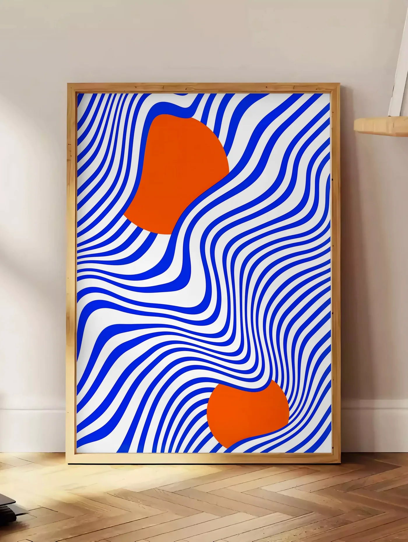 Estampe op Art Bleu et Orange, posee au sol dans un coin salon, sur un parquet a chevrons, pres d'une table d'appoint en chene chargee de livres