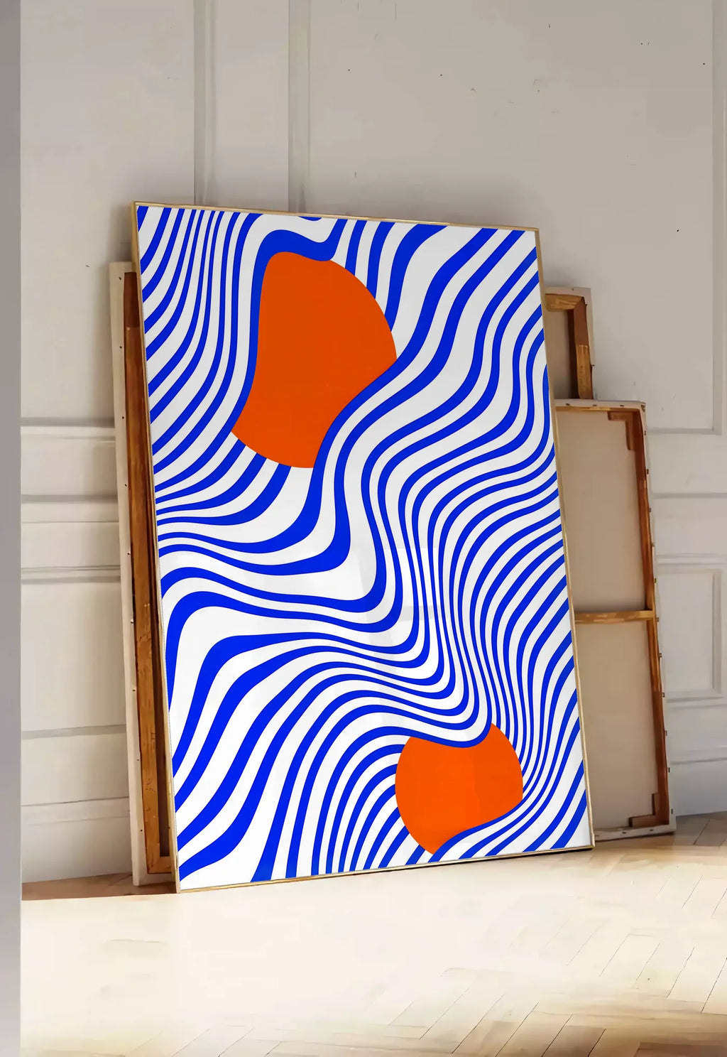 Tirage encadrable op Art Bleu et Orange, posee au sol dans une entree lumineuse, contre un mur a panneaux blancs, a cote de chassis en bois empiles