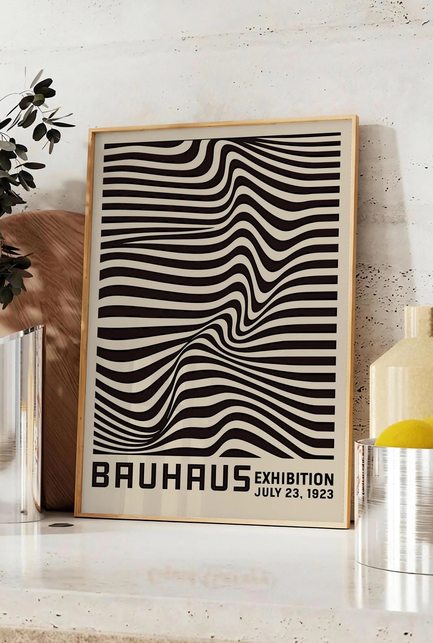 Affiche op Art Vagues Noires, posee sur un plan de travail de cuisine en pierre claire, entre une branche d'eucalyptus en vase et un bocal de citrons