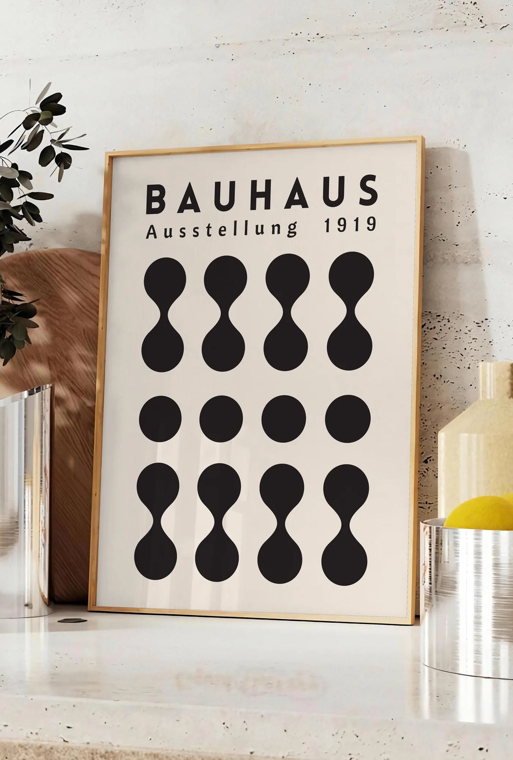 Affiche sabliers et Points, posee sur un plan de travail de cuisine en pierre claire, entre une branche d'eucalyptus en vase et un bocal de citrons
