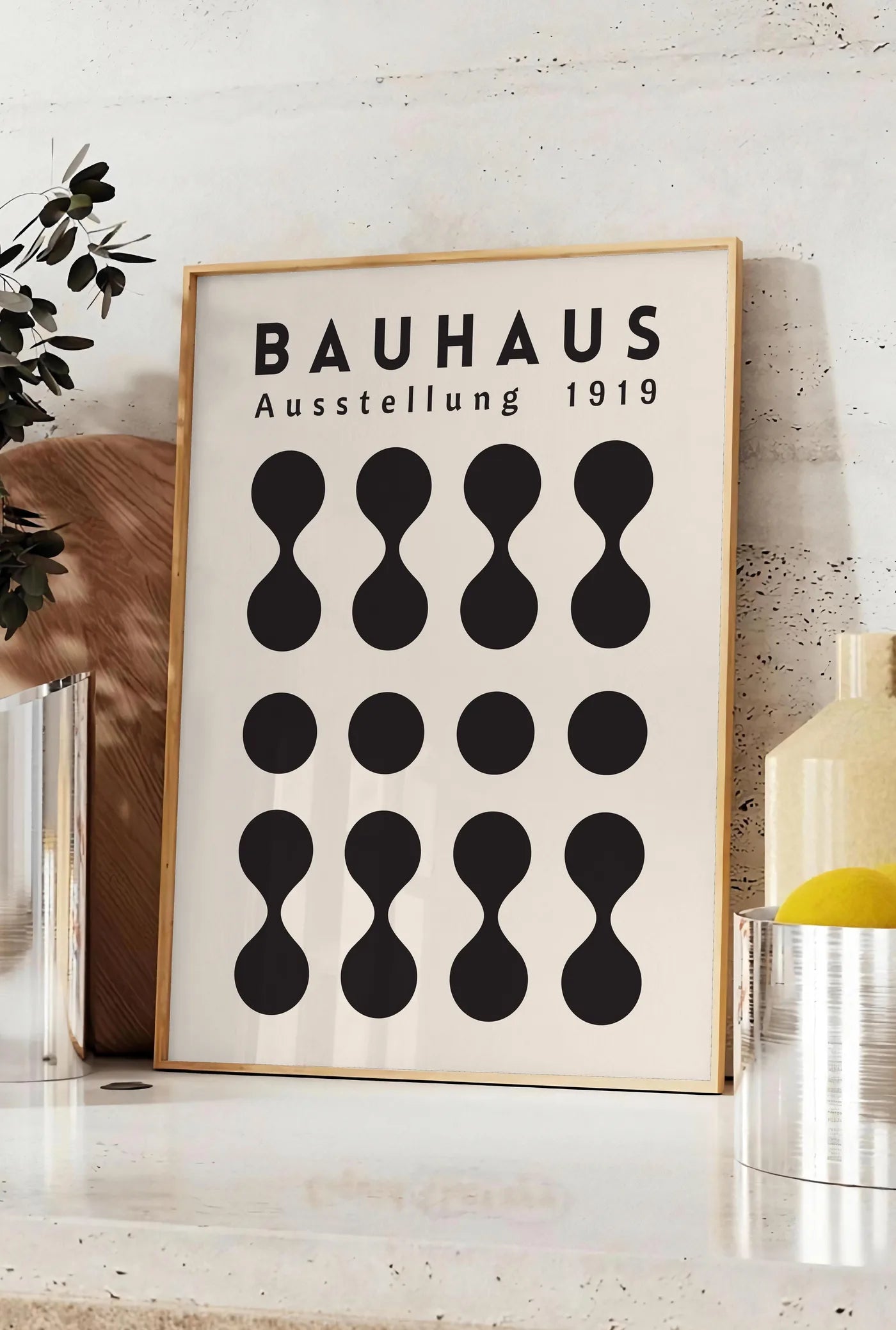 Affiche sabliers et Points, posee sur un plan de travail de cuisine en pierre claire, entre une branche d'eucalyptus en vase et un bocal de citrons