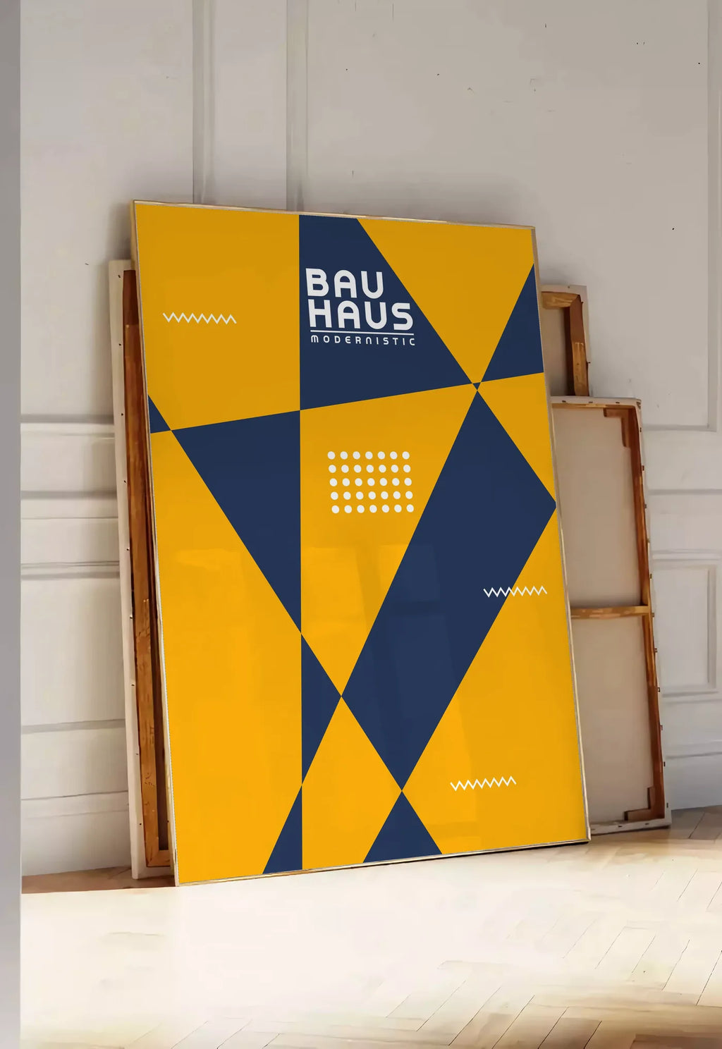 Tirage encadrable triangles Modernistic, posee au sol dans une entree lumineuse, contre un mur a panneaux blancs, a cote de chassis en bois empiles