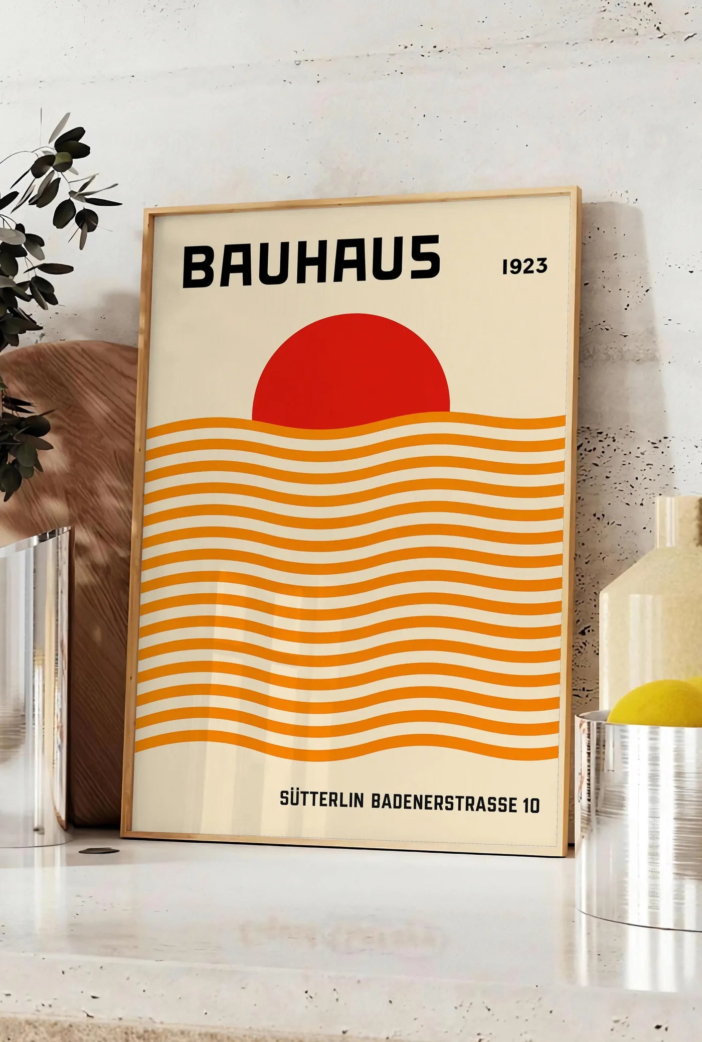 Affiche vagues Orange et Soleil, posee sur un plan de travail de cuisine en pierre claire, entre une branche d'eucalyptus en vase et un bocal de citrons