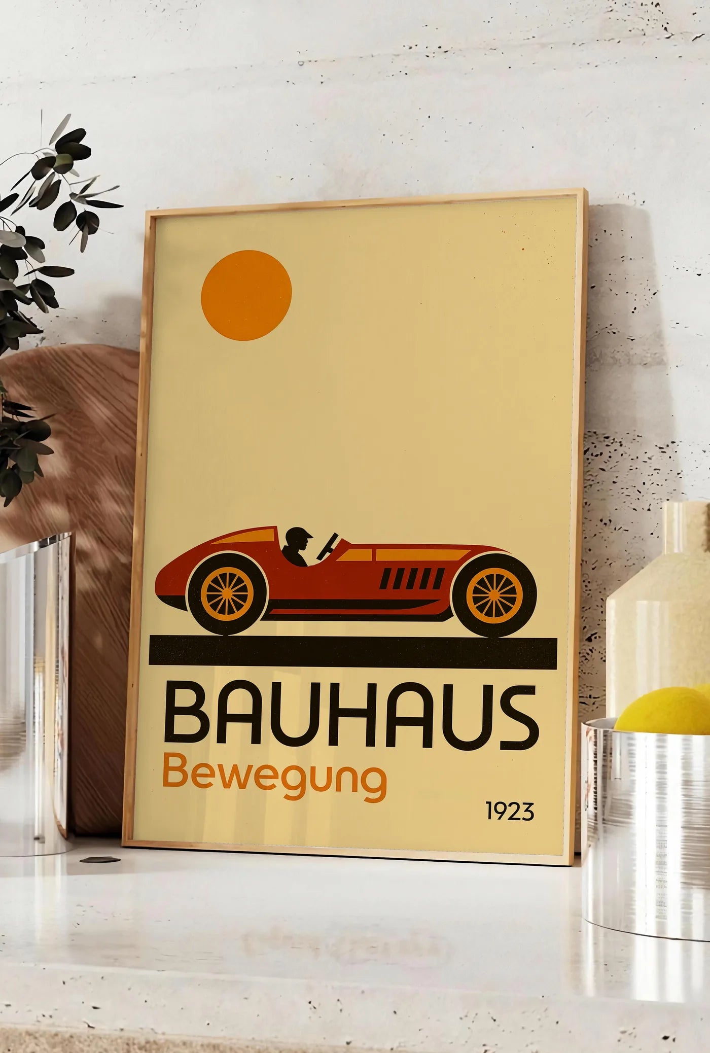 Affiche voiture de Course, posee sur un plan de travail de cuisine en pierre claire, entre une branche d'eucalyptus en vase et un bocal de citrons