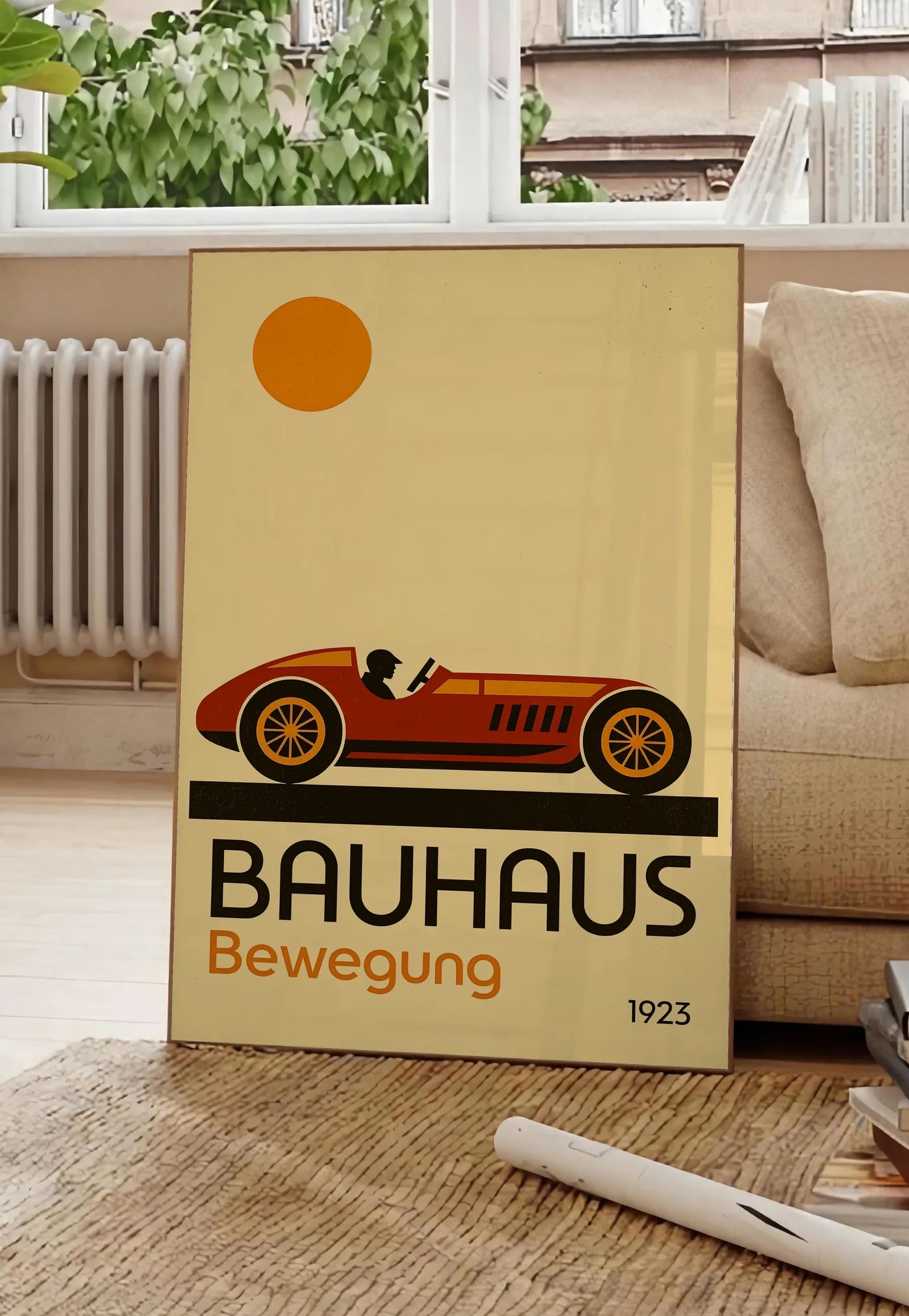 Poster voiture de Course, posee au sol dans un salon parisien, devant une grande fenetre donnant sur un immeuble haussmannien, entre un ficus et un canape creme