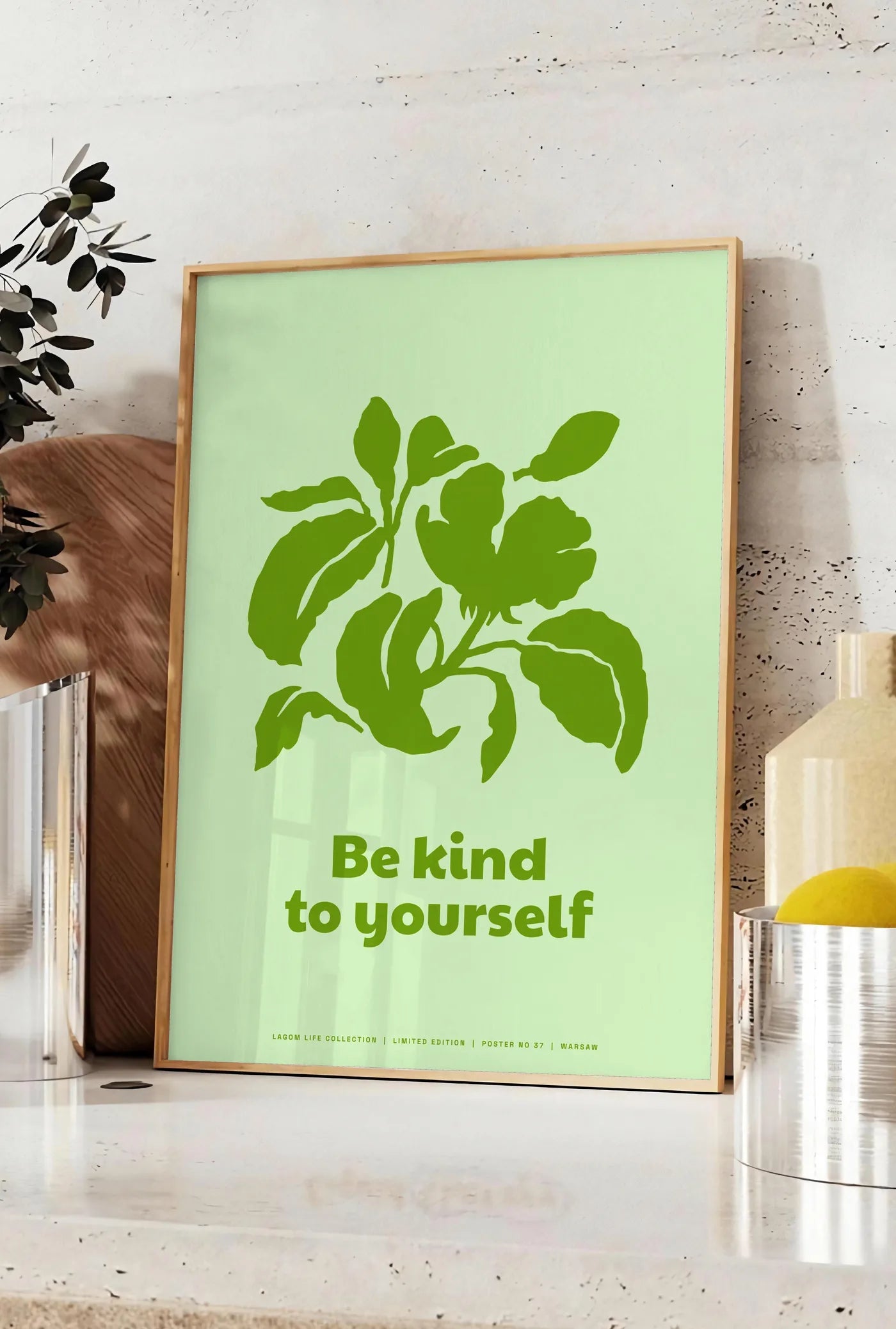 Affiche affiche feuillage vert, posee sur un plan de travail de cuisine en pierre claire, entre une branche d'eucalyptus en vase et un bocal de citrons