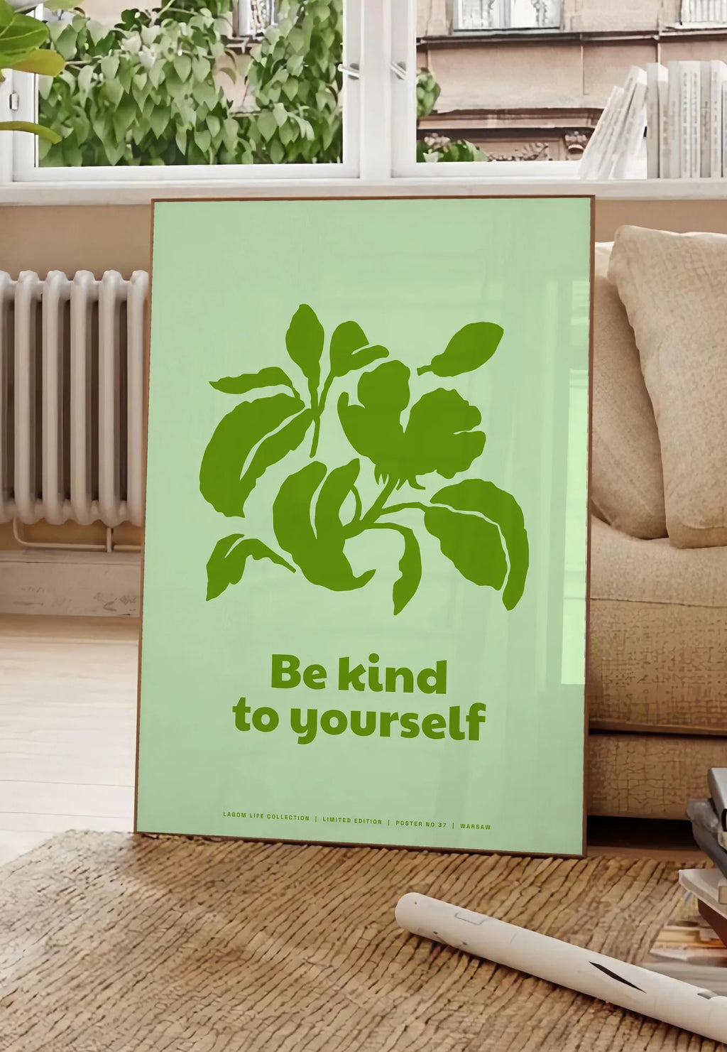 Poster affiche feuillage vert, posee au sol dans un salon parisien, devant une grande fenetre donnant sur un immeuble haussmannien, entre un ficus et un canape creme