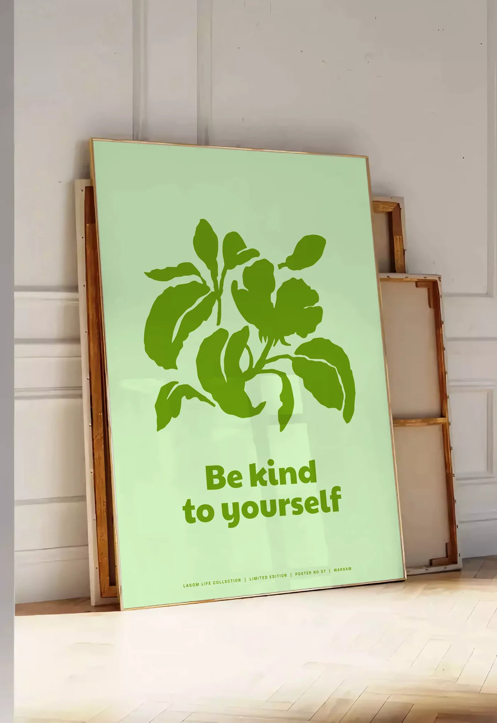 Tirage encadrable affiche feuillage vert, posee au sol dans une entree lumineuse, contre un mur a panneaux blancs, a cote de chassis en bois empiles