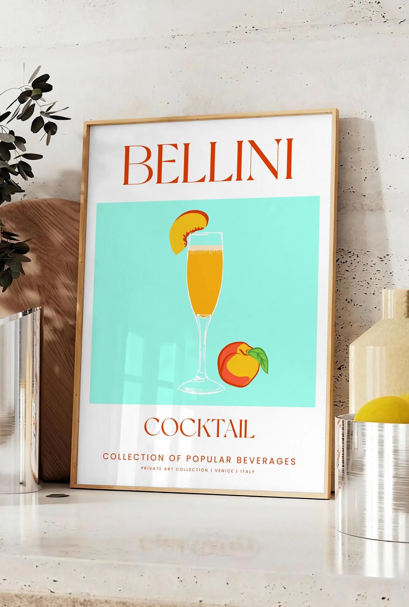 Affiche affiche cocktail Bellini, posee sur un plan de travail de cuisine en pierre claire, entre une branche d'eucalyptus en vase et un bocal de citrons
