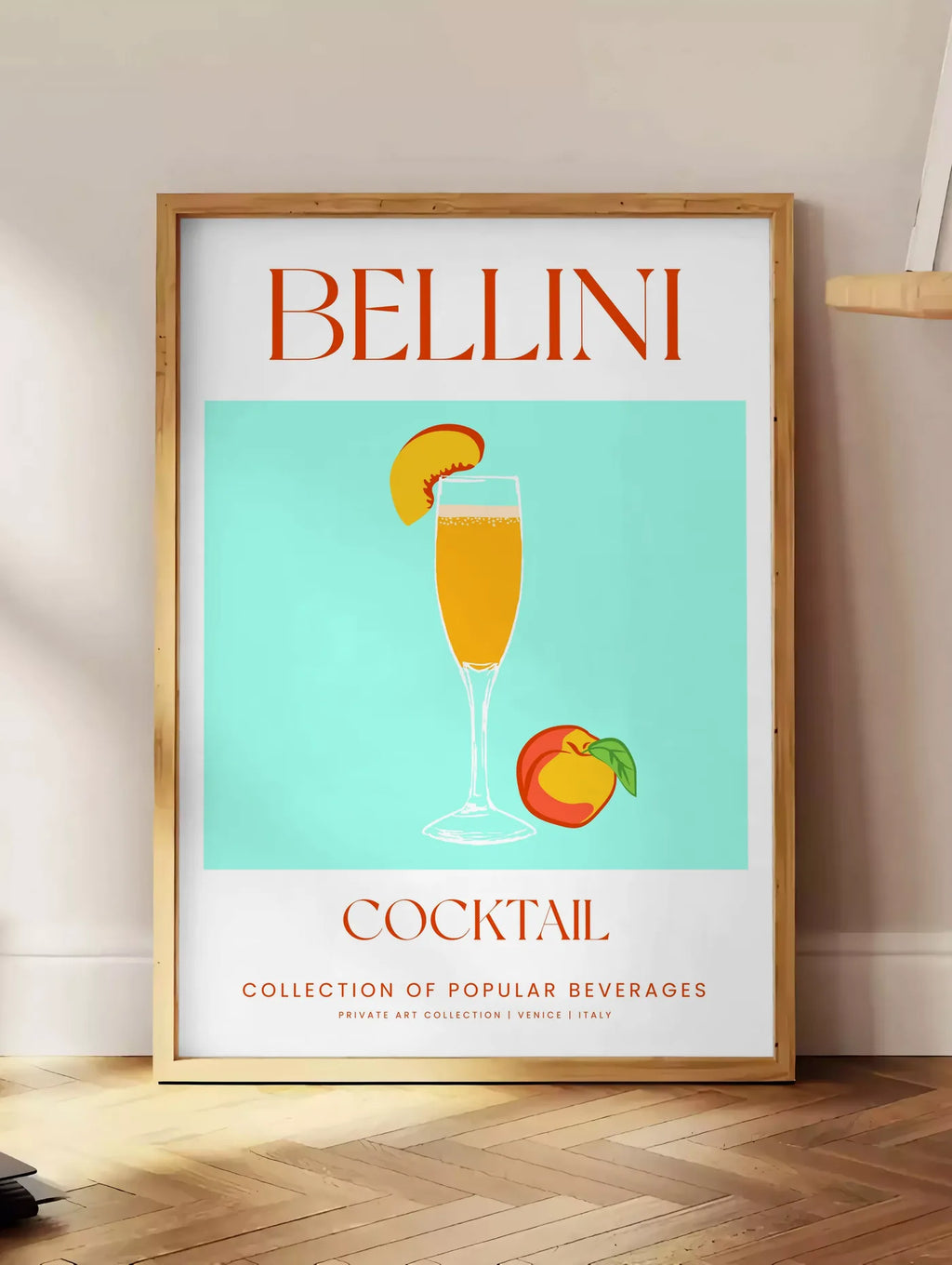 Estampe affiche cocktail Bellini, posee au sol dans un coin salon, sur un parquet a chevrons, pres d'une table d'appoint en chene chargee de livres