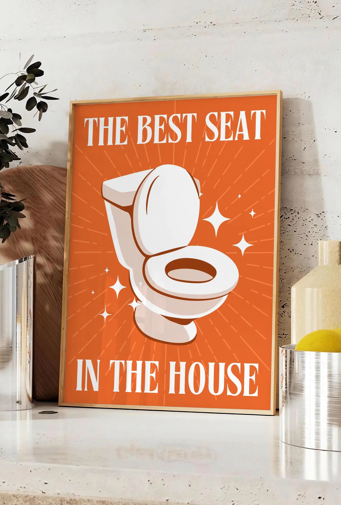 Affiche affiche toilettes humour, posee sur un plan de travail de cuisine en pierre claire, entre une branche d'eucalyptus en vase et un bocal de citrons