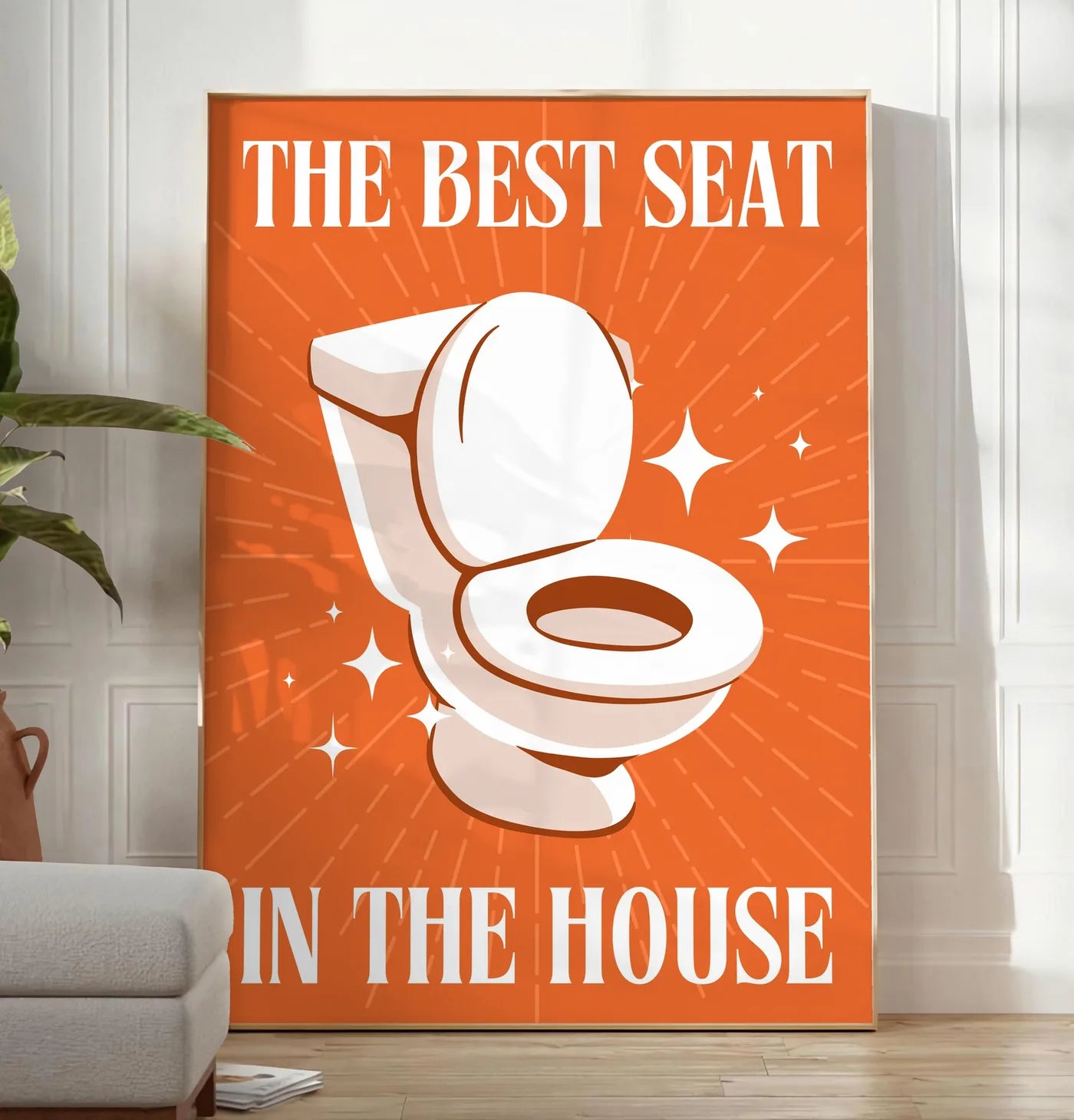 Reproduction affiche toilettes humour, posee au sol dans un salon minimaliste clair, a cote d'un canape beige et d'une plante verte, sur un parquet clair