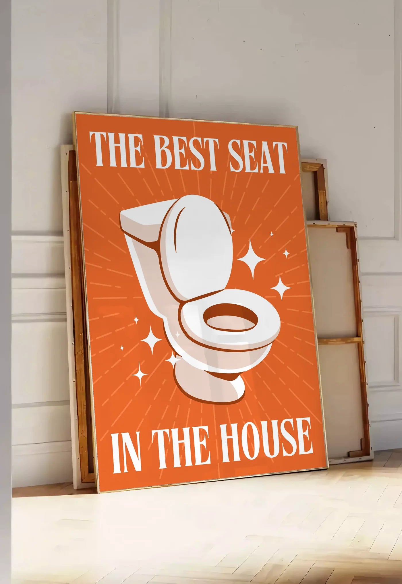 Tirage encadrable affiche toilettes humour, posee au sol dans une entree lumineuse, contre un mur a panneaux blancs, a cote de chassis en bois empiles