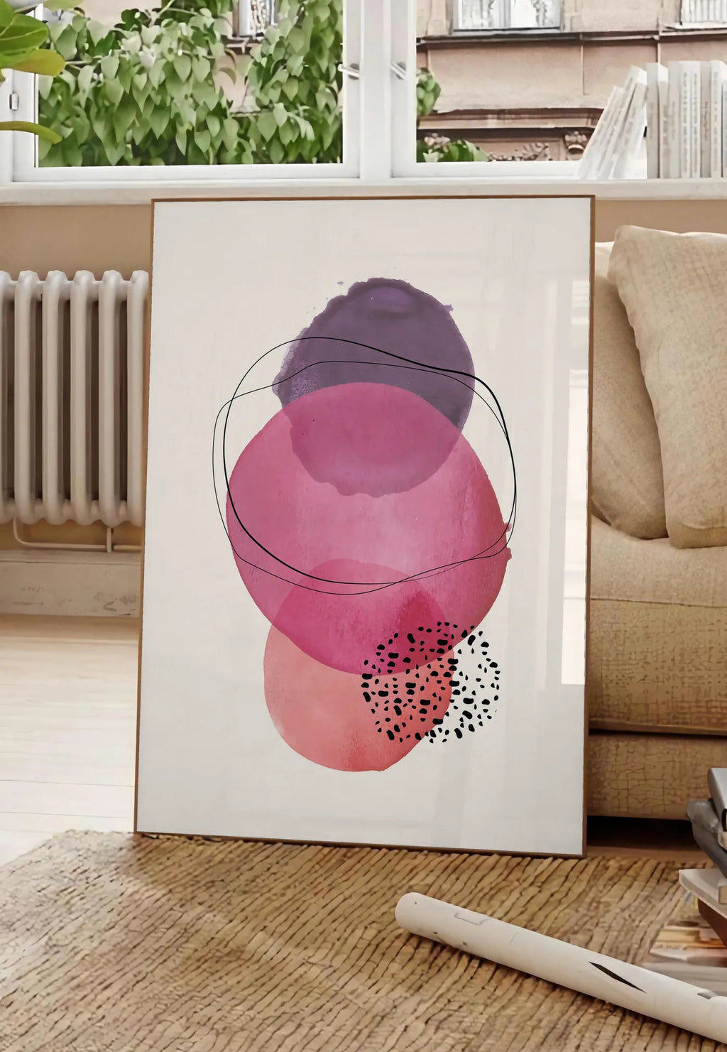 Poster cercles aquarelle roses magenta et violets superposes sur creme, posee au sol dans un salon parisien, devant une grande fenetre donnant sur un immeuble haussmannien, entre un ficus et un canape creme